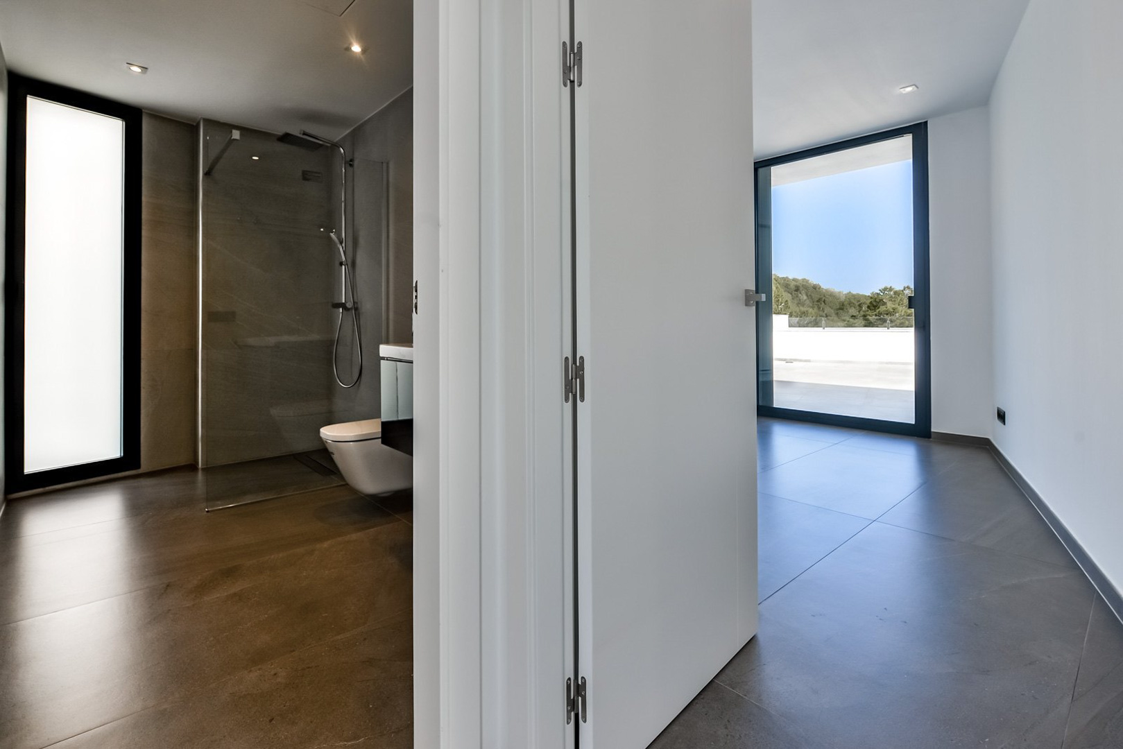 Master bedroom with en-suite bathroom featuring a walk-in shower, large-format tiling, and floor-to-ceiling glass doors leading to the private terrace.