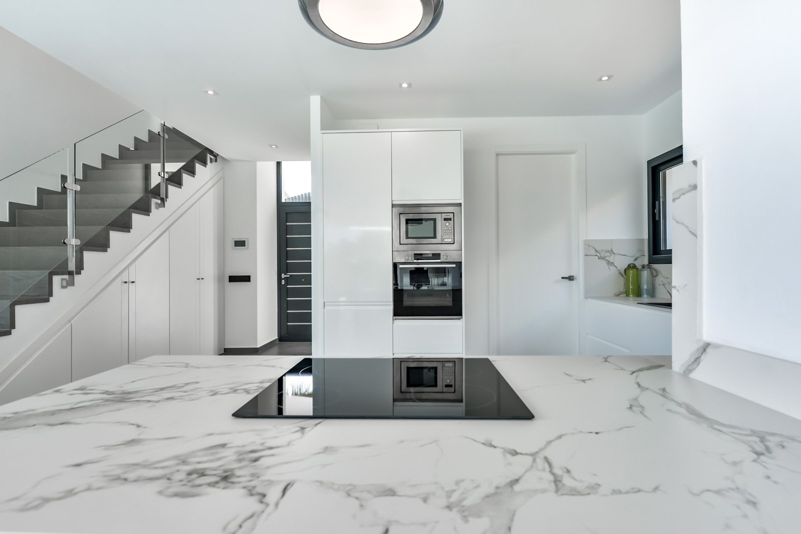 Modern kitchen featuring a marble-effect countertop with induction hob, adjacent to a contemporary staircase with glass balustrade and integrated storage.