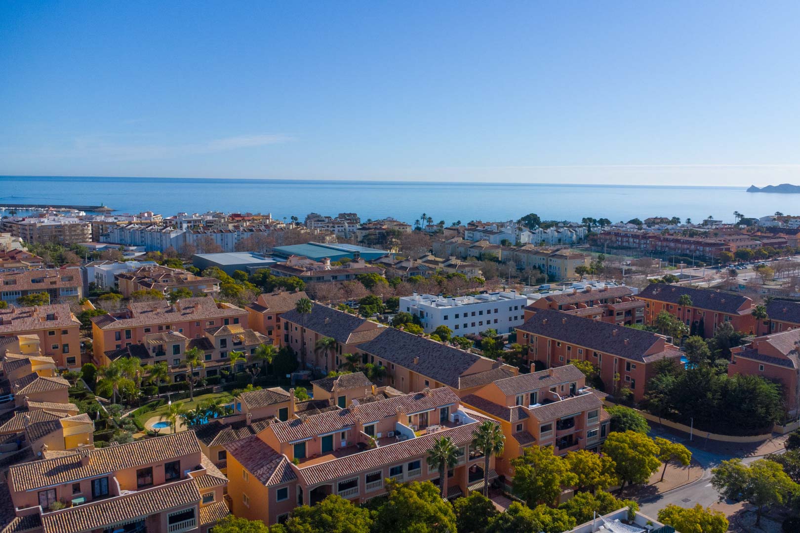 Aerial view of the Floridamar complex in Jávea, highlighting the Mediterranean architecture, communal gardens, and its proximity to the coastline and port.