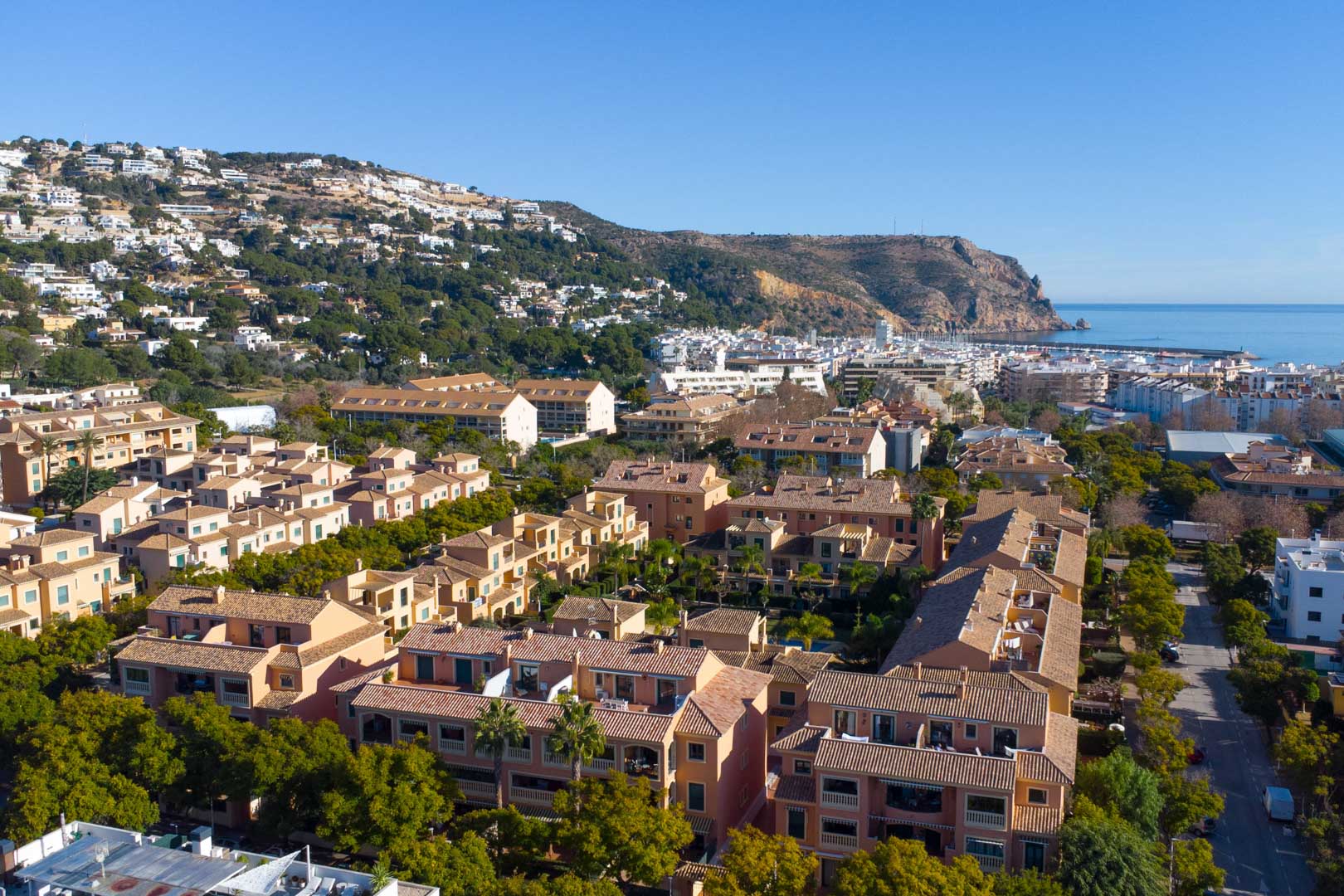 Aerial view of the Floridamar complex in Jávea, showcasing terracotta architecture, lush greenery, and its prime location near the port and sea.