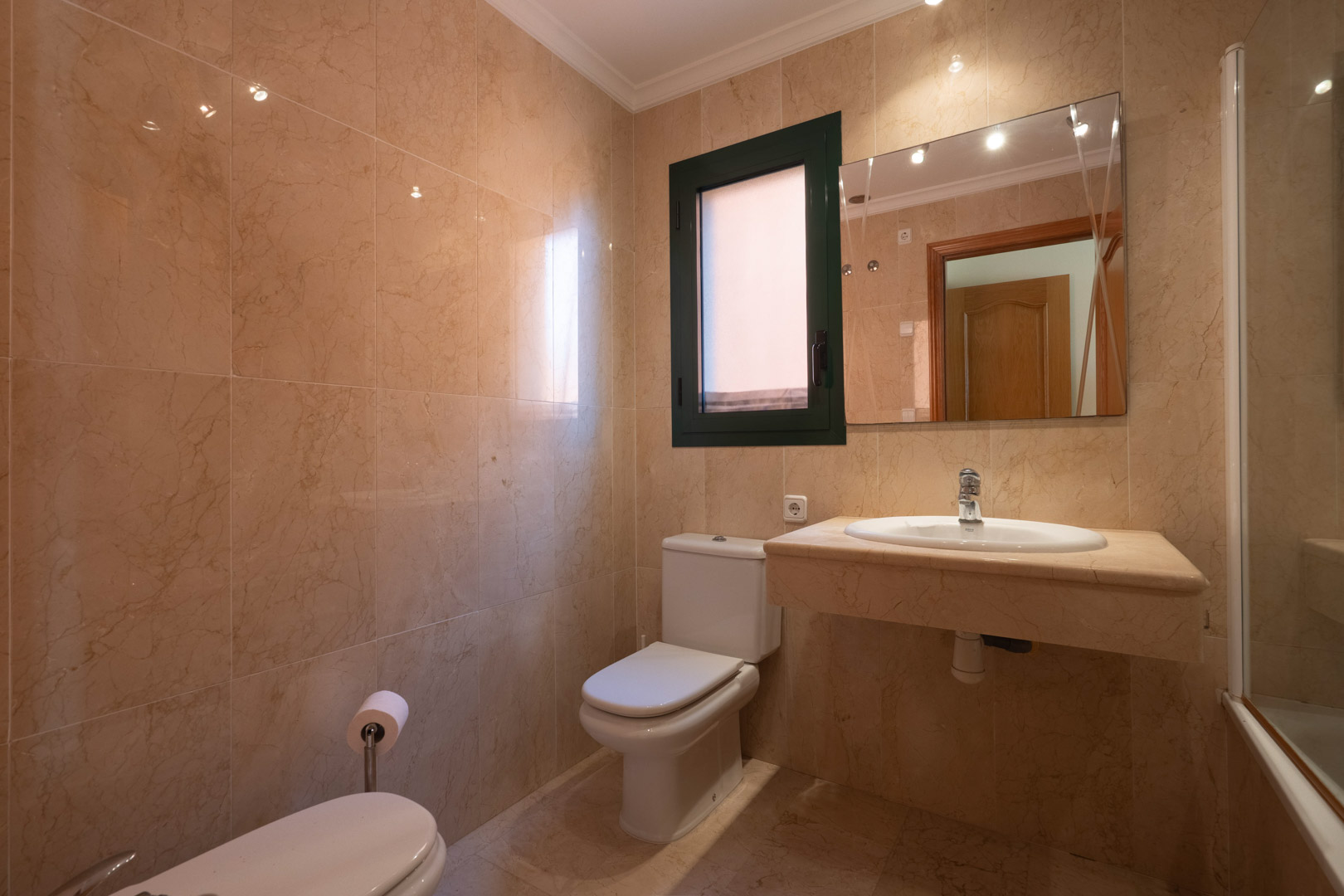 Bathroom featuring full-height cream marble tiling, an integrated stone vanity with inset basin, and a window providing natural light and ventilation.