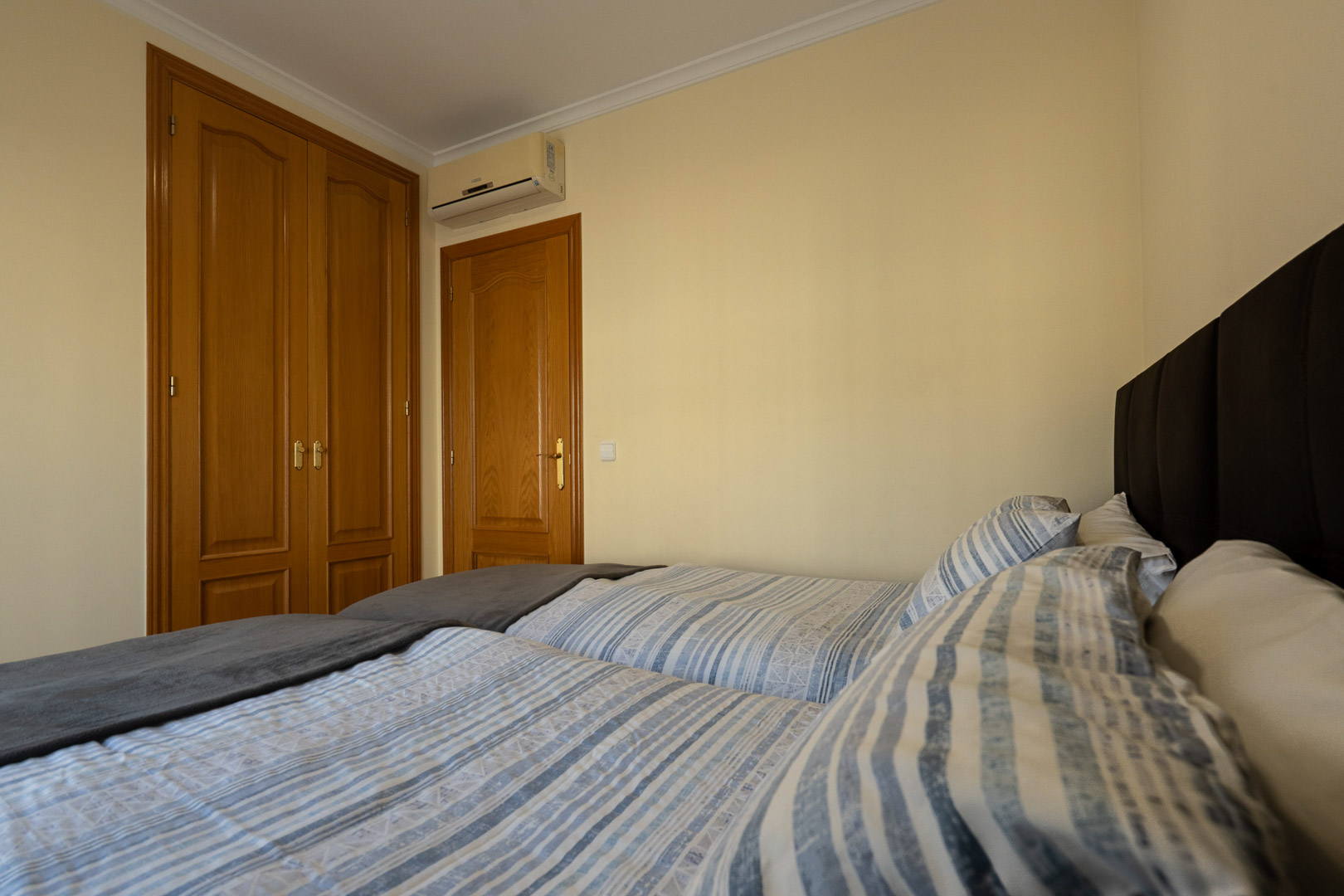 Bedroom featuring classic built-in wooden wardrobes, split system air conditioning, and beds with a dark upholstered headboard.