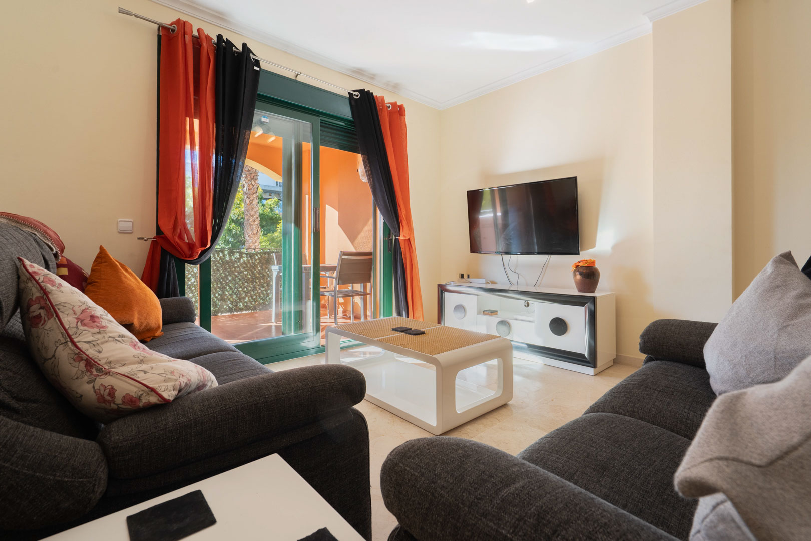 Bright living area featuring dark grey sofas, marble flooring, and direct access to a private terrace through large sliding glass doors.