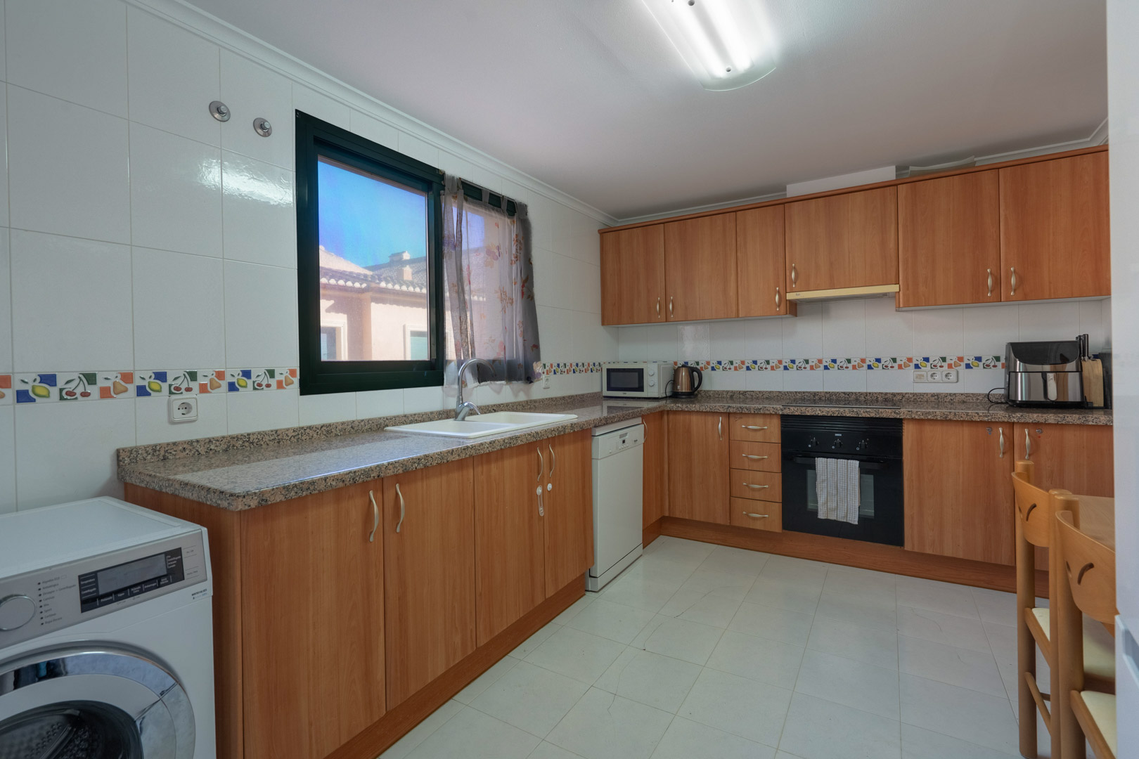 Functional kitchen with wooden cabinetry, granite countertops, decorative tile borders, and full appliances including a washing machine and dishwasher.
