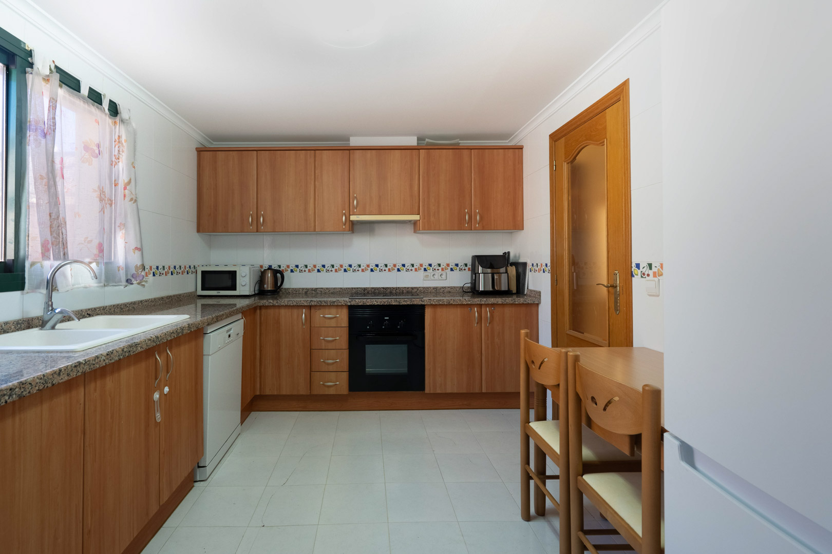 Independent kitchen featuring wood cabinetry, granite countertops, and integrated appliances. The space includes a compact dining area and walls finished with decorative tiling.