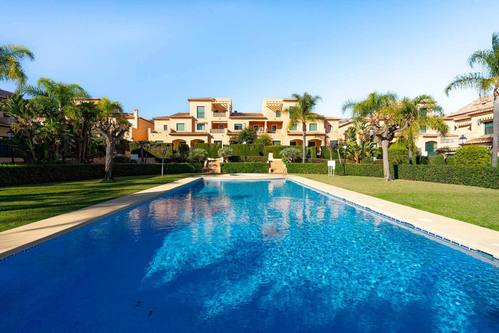 Large outdoor swimming pool set within manicured lawns and Mediterranean gardens, featuring the traditional terracotta architecture of the Floridamar complex.