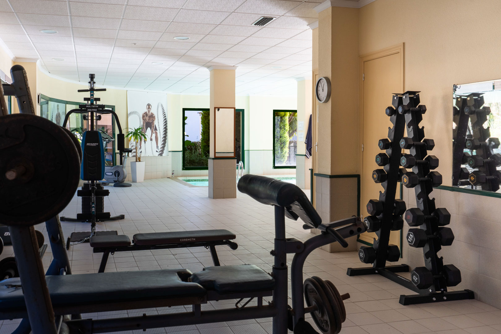 Resident gym featuring weight machines, a dumbbell rack, and benches, conveniently located adjacent to the indoor heated pool area.