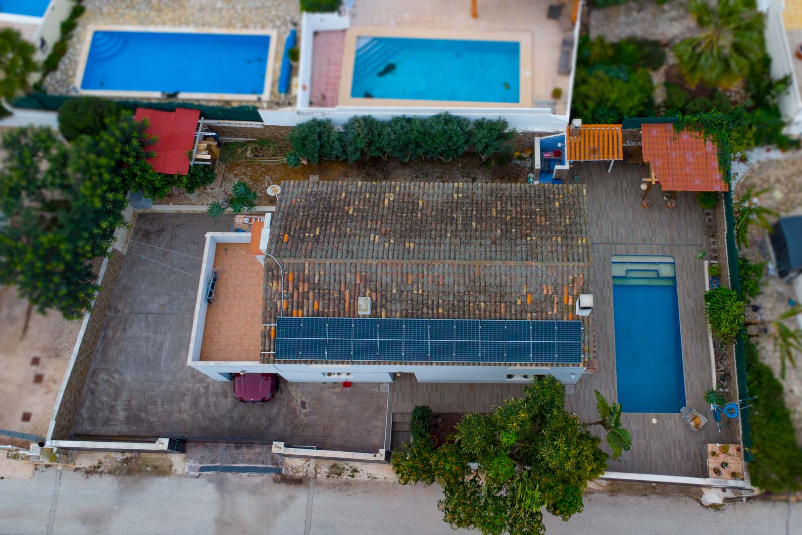 Aerial perspective showing the rooftop solar panel installation, a rectangular swimming pool with tiled decking, and the private driveway.