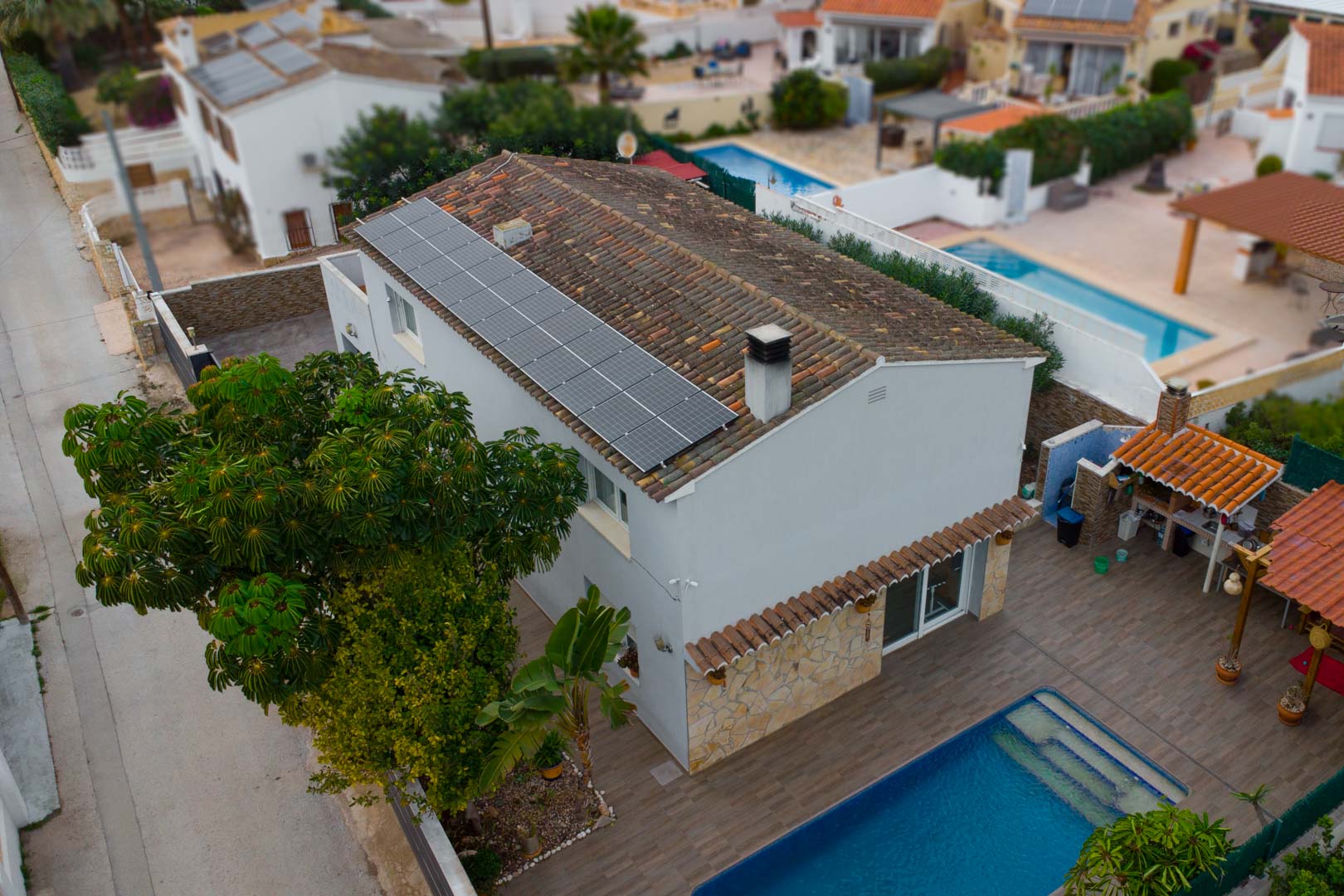 Aerial view of the villa featuring roof-mounted solar panels, a private swimming pool, and an outdoor kitchen area set within a tiled terrace.