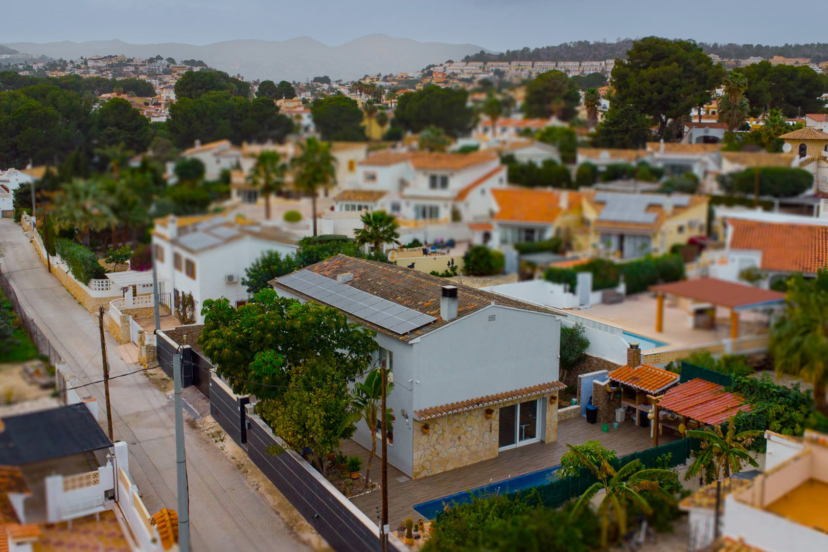 Aerial view of the villa featuring rooftop solar panels, a private pool, and a covered outdoor kitchen within a residential setting in Calpe.