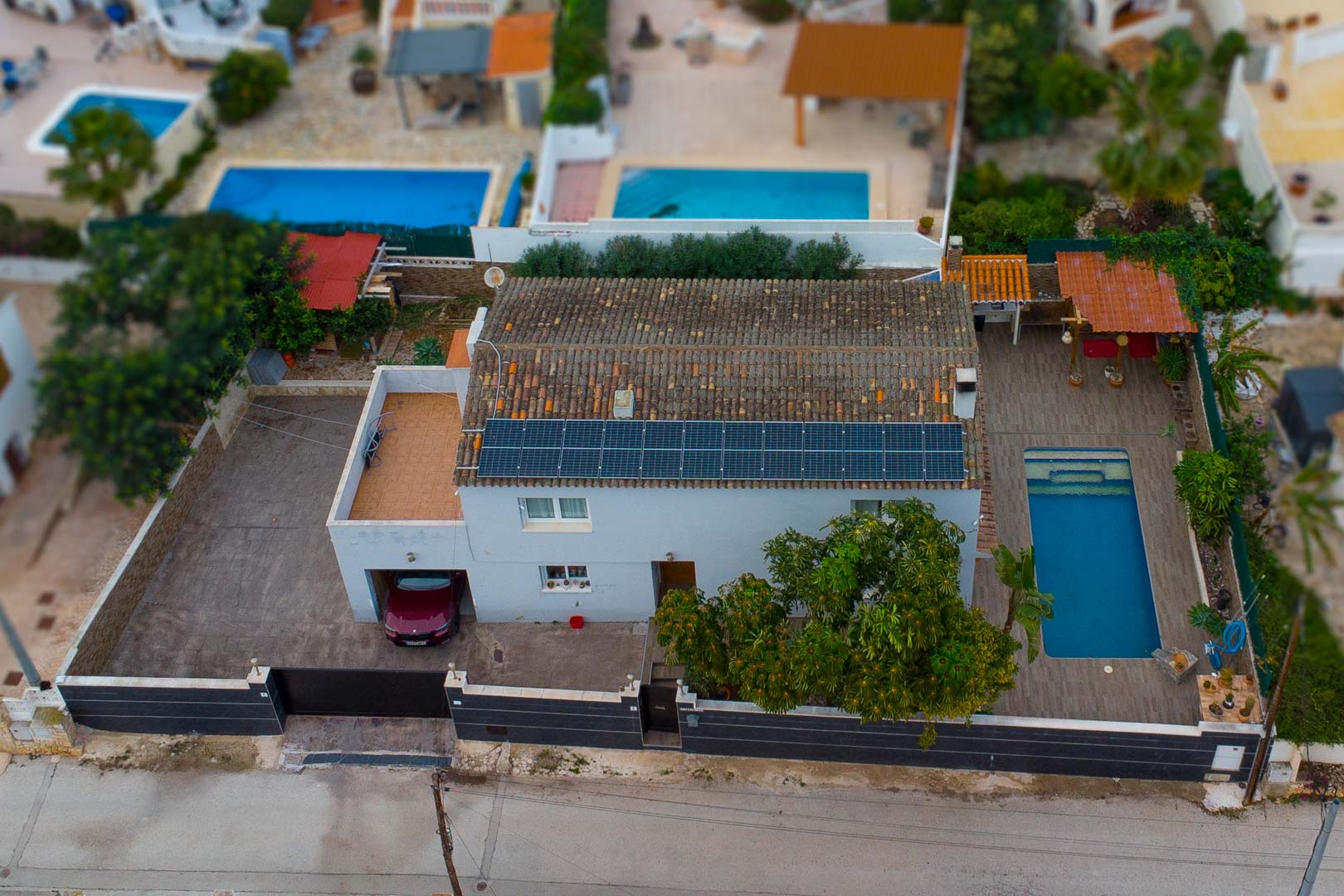 Aerial view of the villa featuring rooftop solar panels, a private swimming pool with a sun terrace, and an integrated garage on a secure, fenced plot.