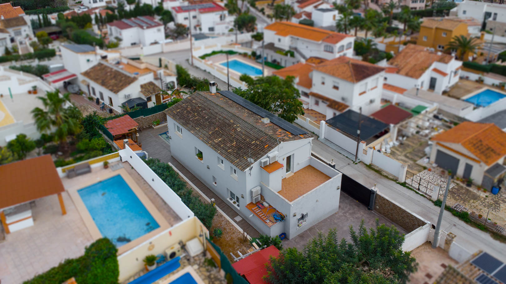 Aerial view of the villa featuring rooftop solar panels, a terracotta-tiled upper terrace, and its position within a quiet residential neighborhood.