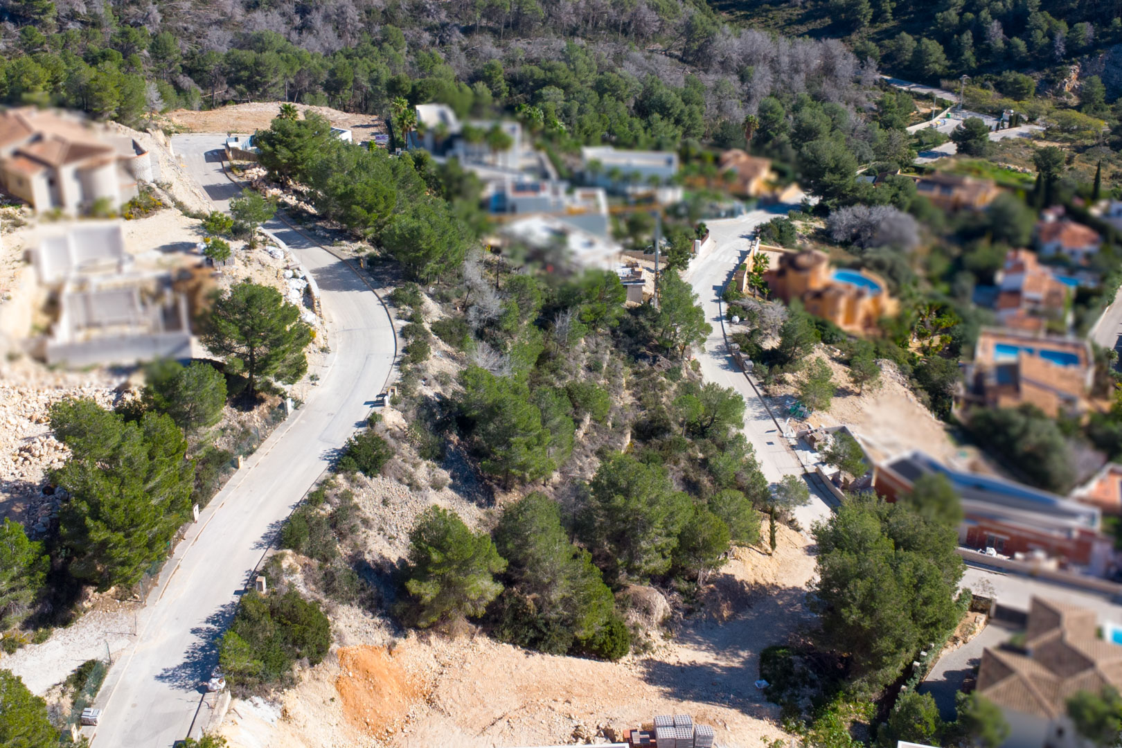 Aerial view of the Tosalet 5 urbanization in Jávea, featuring paved access roads, sloped building plots with pine trees, and established villas in the background.