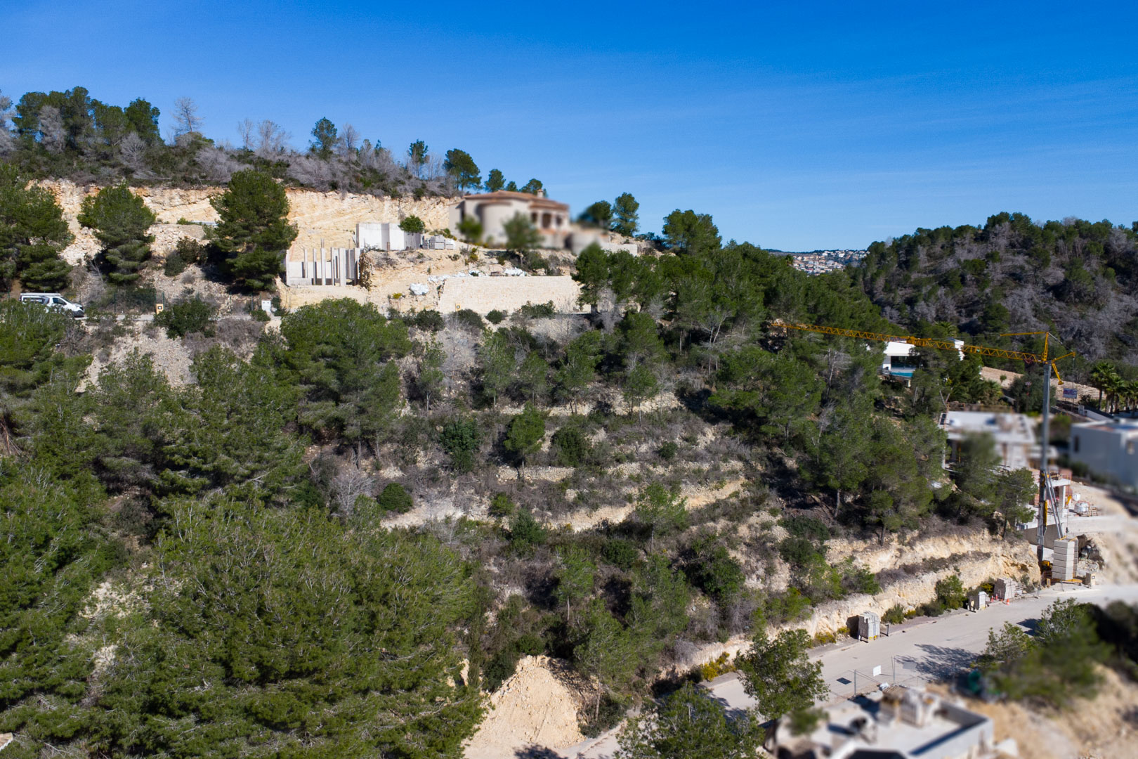 Elevated view of a terraced hillside plot featuring Mediterranean pine trees, stone retaining walls, and ongoing construction in Tosalet 5.