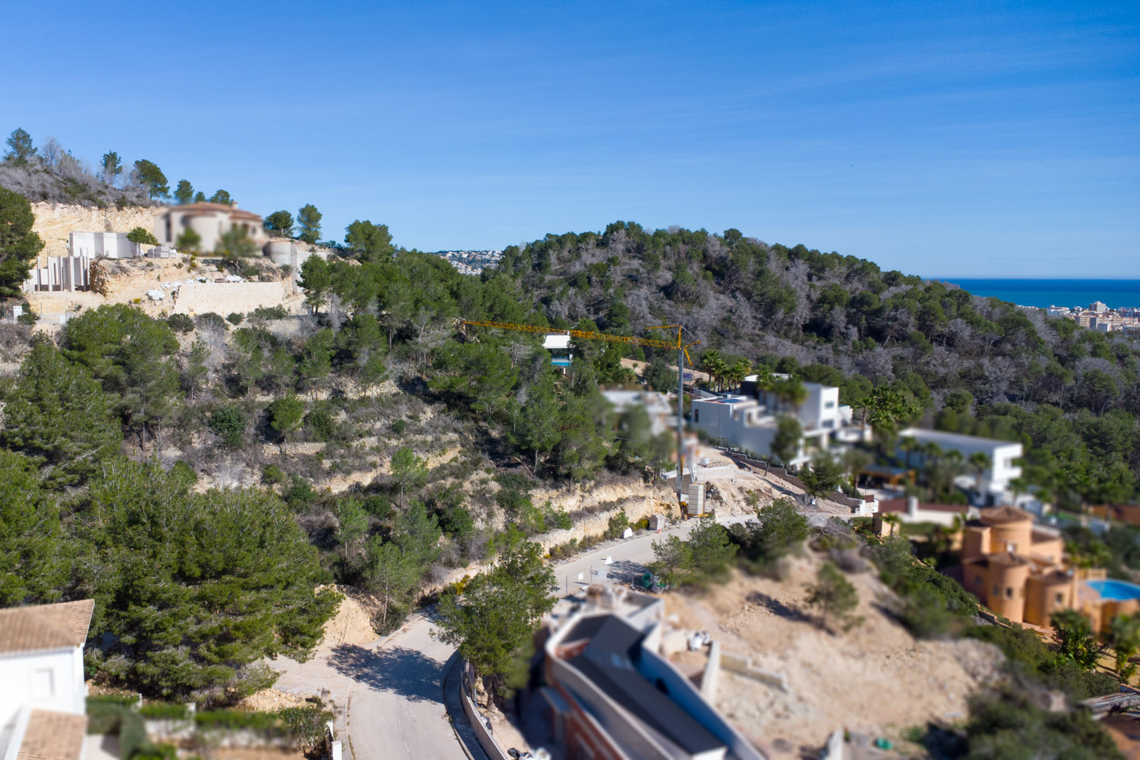 Elevated view of the Tosalet 5 urbanization in Jávea, featuring sloped plots integrated into a pine forest with distant Mediterranean Sea views.