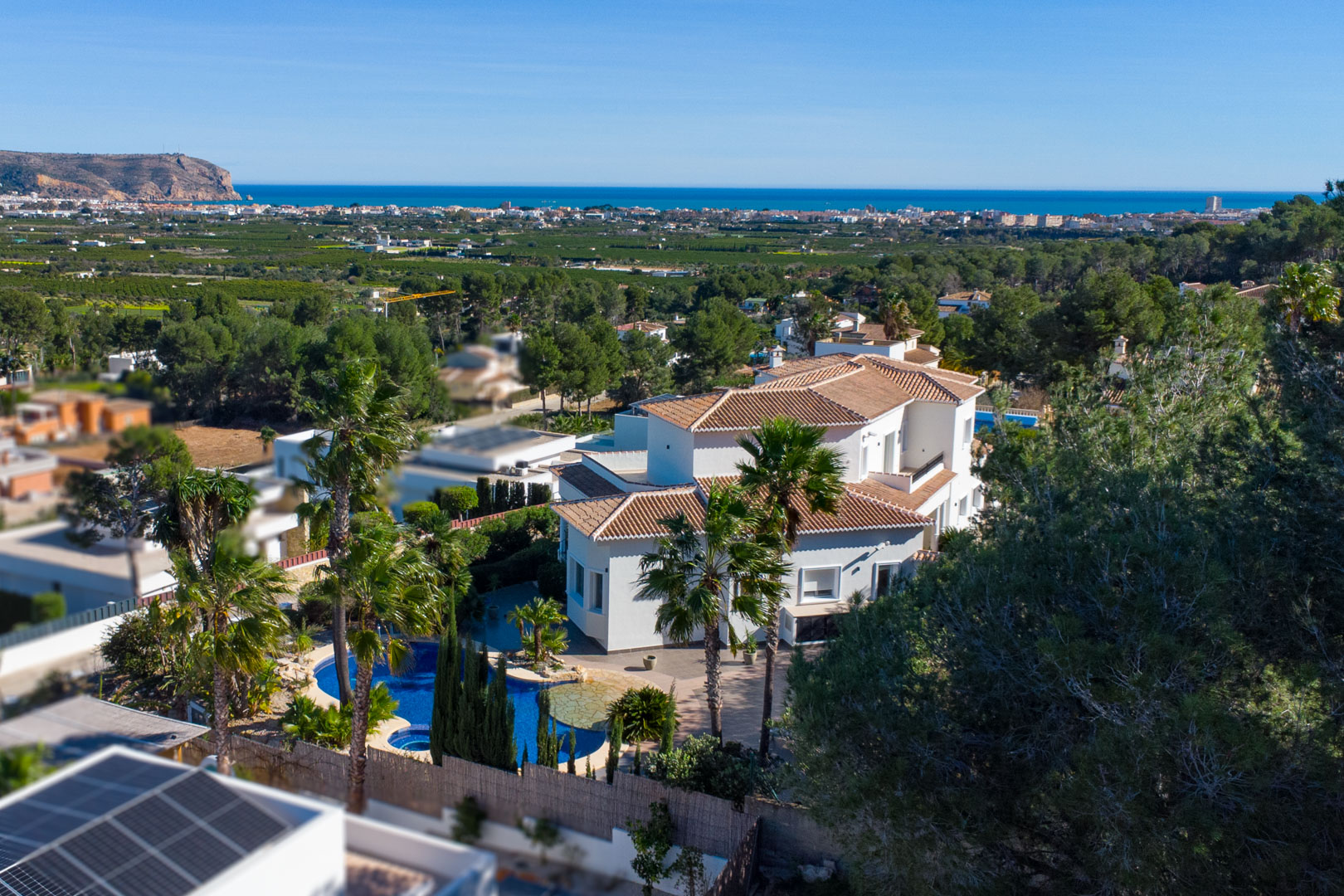 Aerial perspective of the white villa featuring a private pool with integrated jacuzzi, tropical landscaping, and expansive views of the Mediterranean coastline.