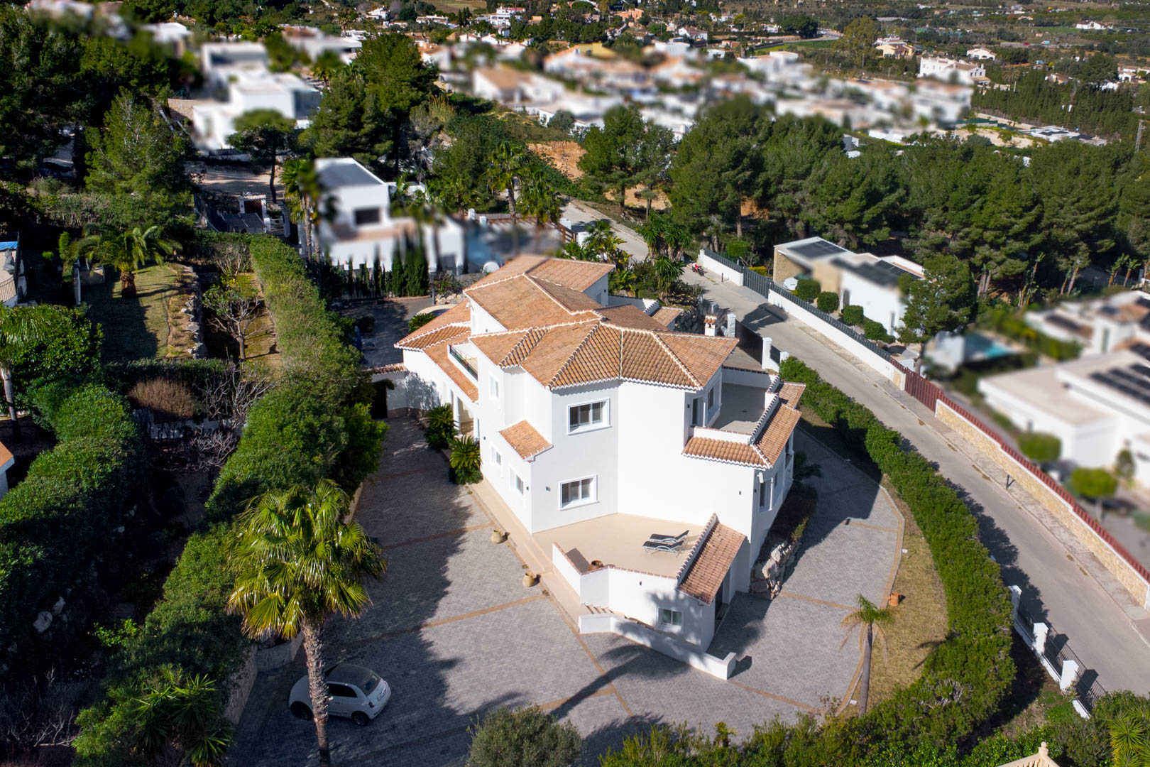 Aerial view of the white villa featuring traditional tile roofing, a spacious paved driveway, and multiple private terraces set within a Mediterranean landscape.