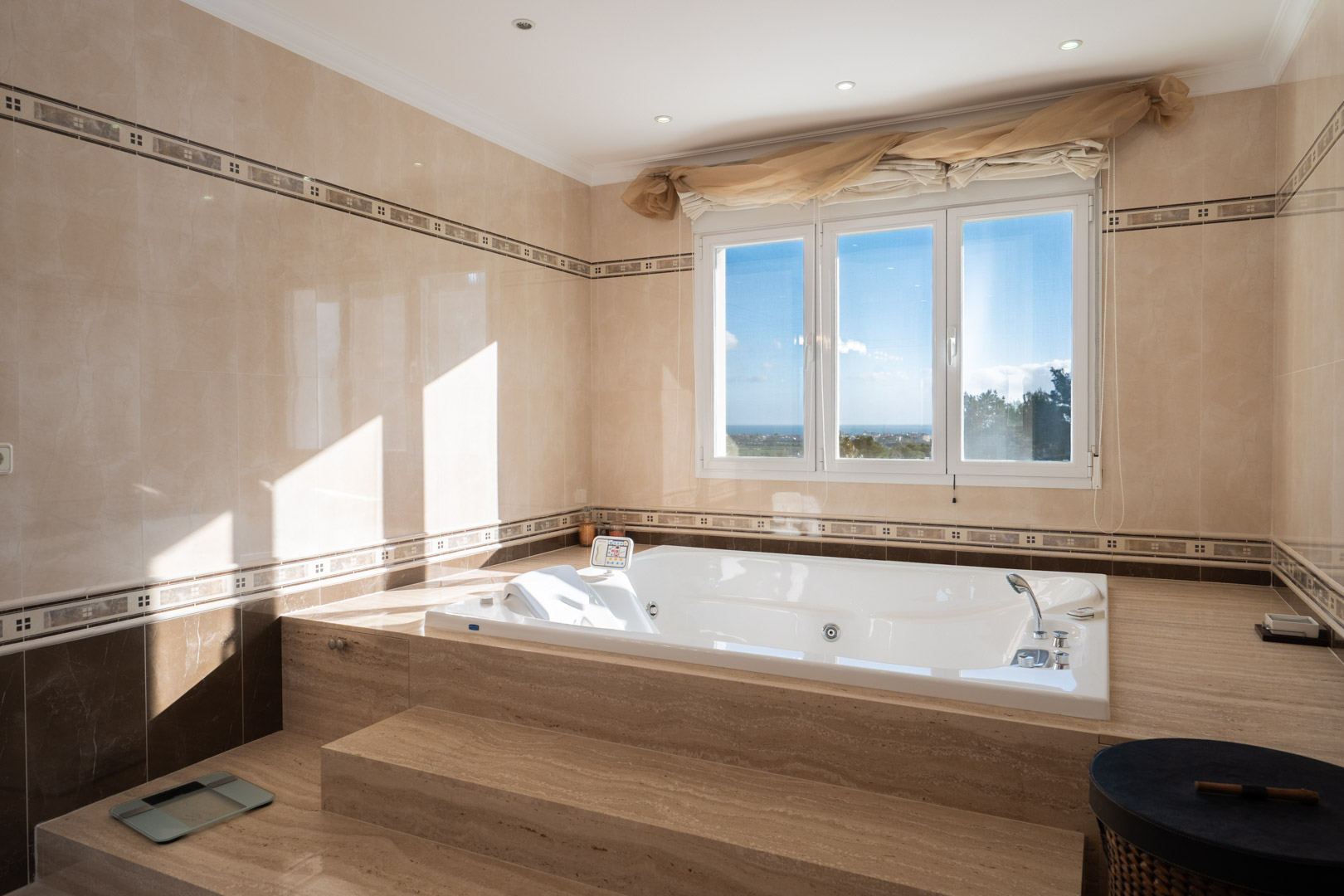 Bathroom featuring a built-in hydromassage tub set in marble steps, with a large window offering panoramic sea views and abundant natural light.