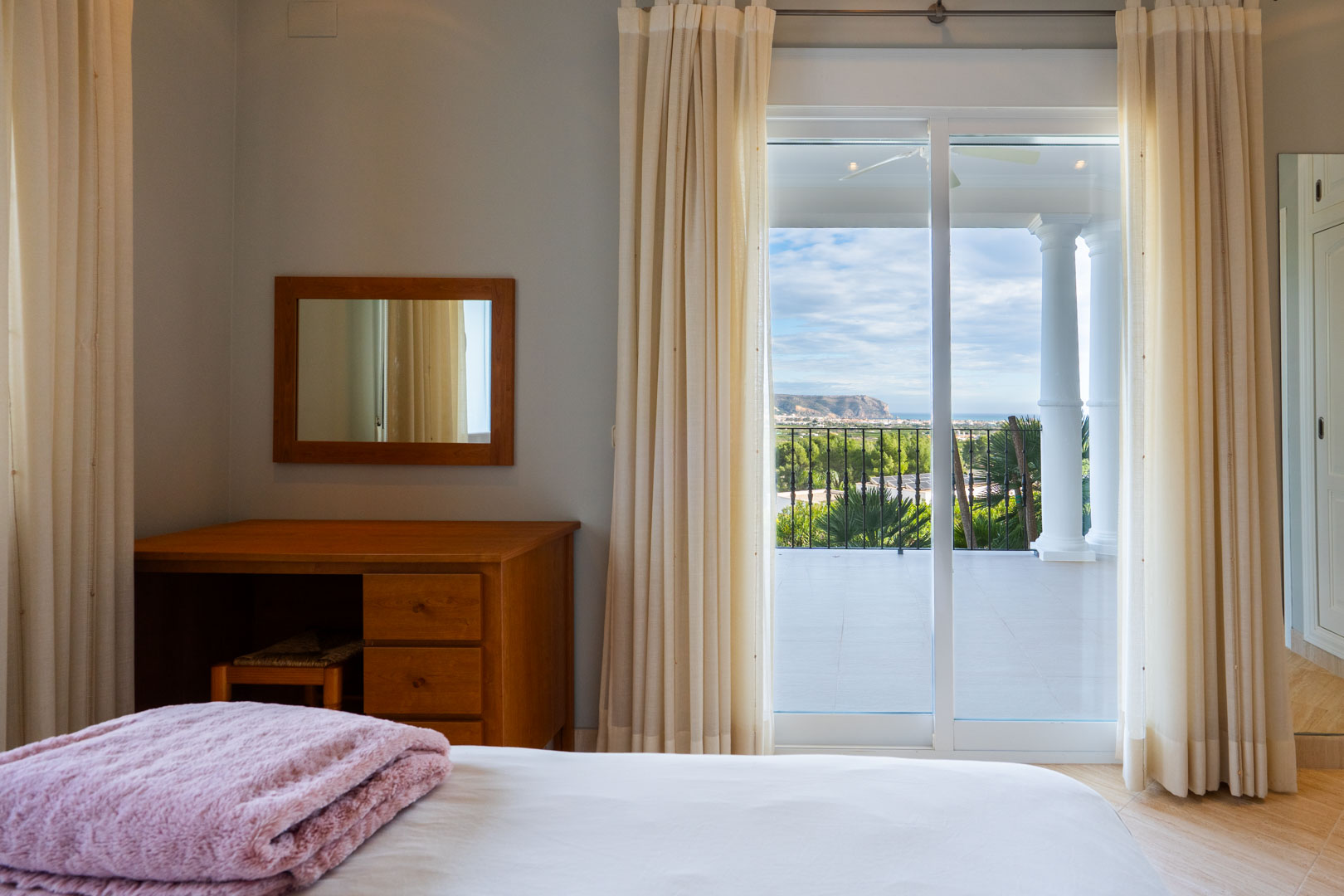 Bedroom featuring a wooden vanity and sliding glass doors opening to a private terrace with white columns and views of the Montgó mountain.