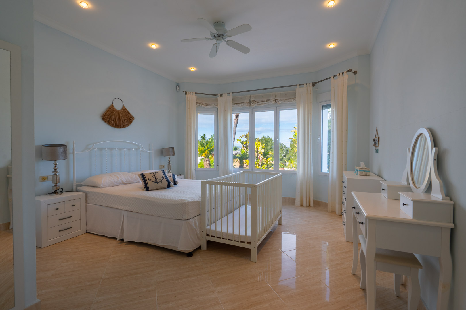 Bedroom featuring polished tile floors, a bay window with garden views, white classic furniture, a vanity desk, and a ceiling fan.