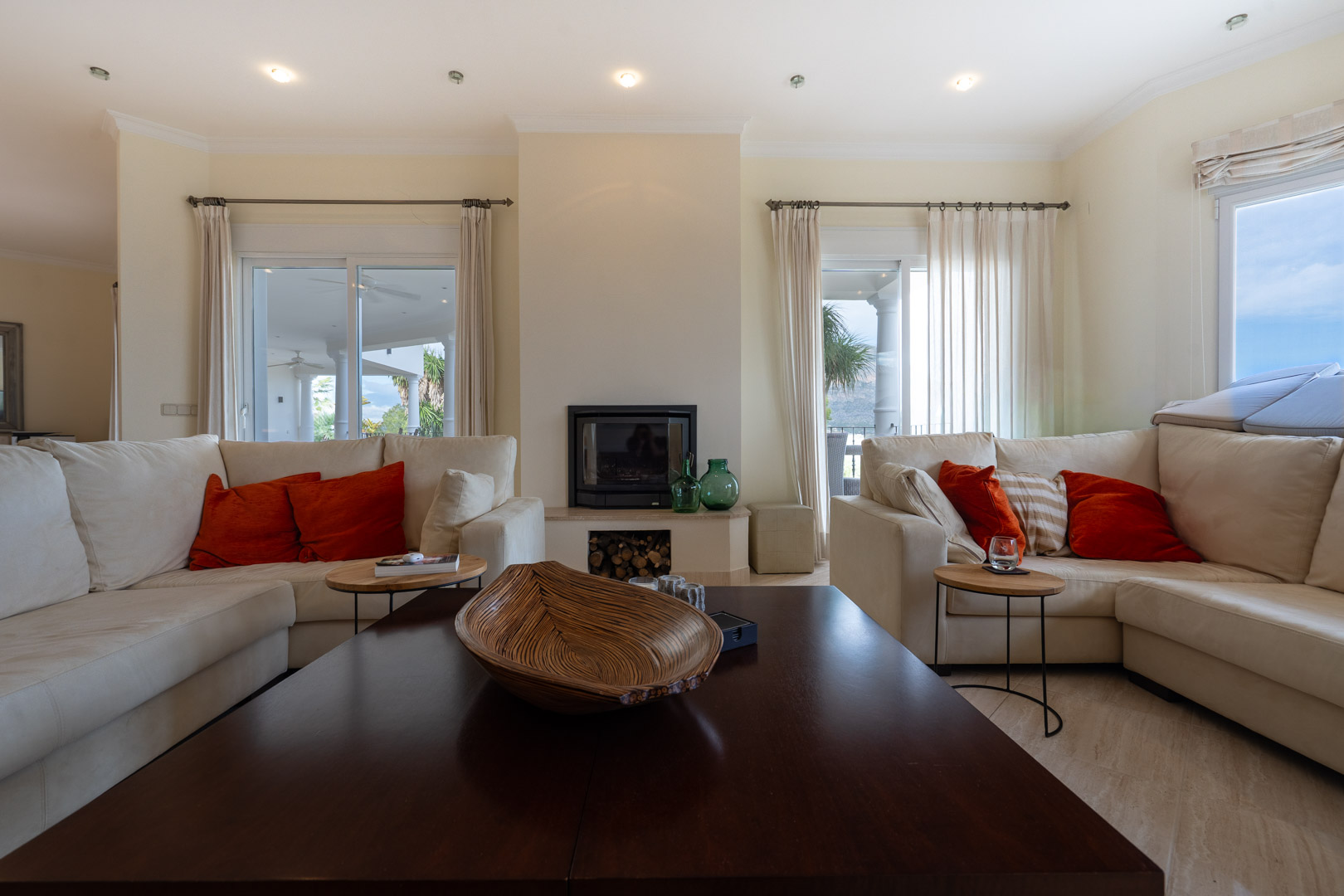 Bright living room featuring a central fireplace, cream-colored sofas with orange accents, and direct access to the terrace through sliding glass doors.