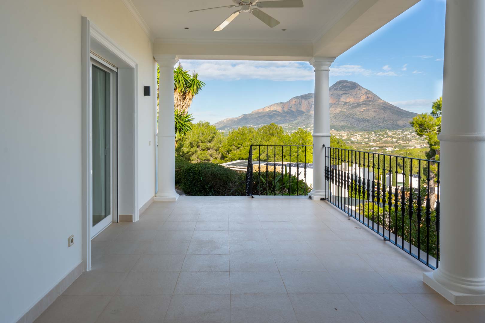 Covered master suite terrace featuring classical white columns, wrought-iron railings, and panoramic views of the Montgó mountain and valley.
