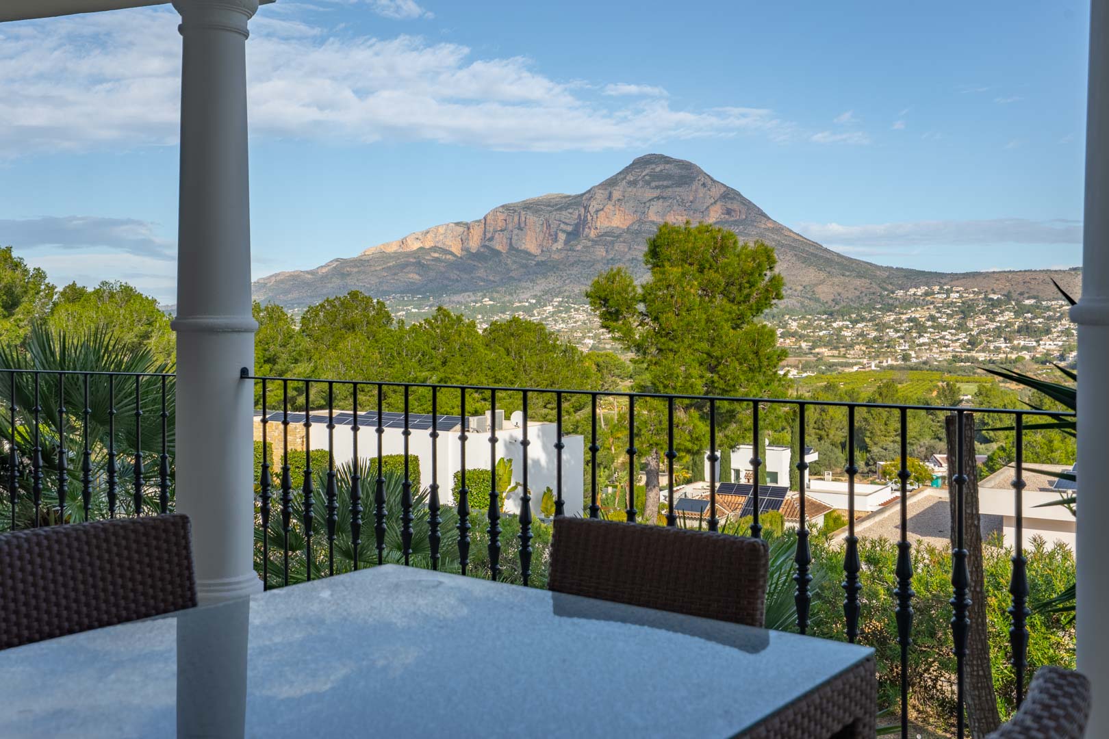 Covered terrace featuring an outdoor dining area with a stone tabletop and wrought iron railings, overlooking the Montgó mountain range.