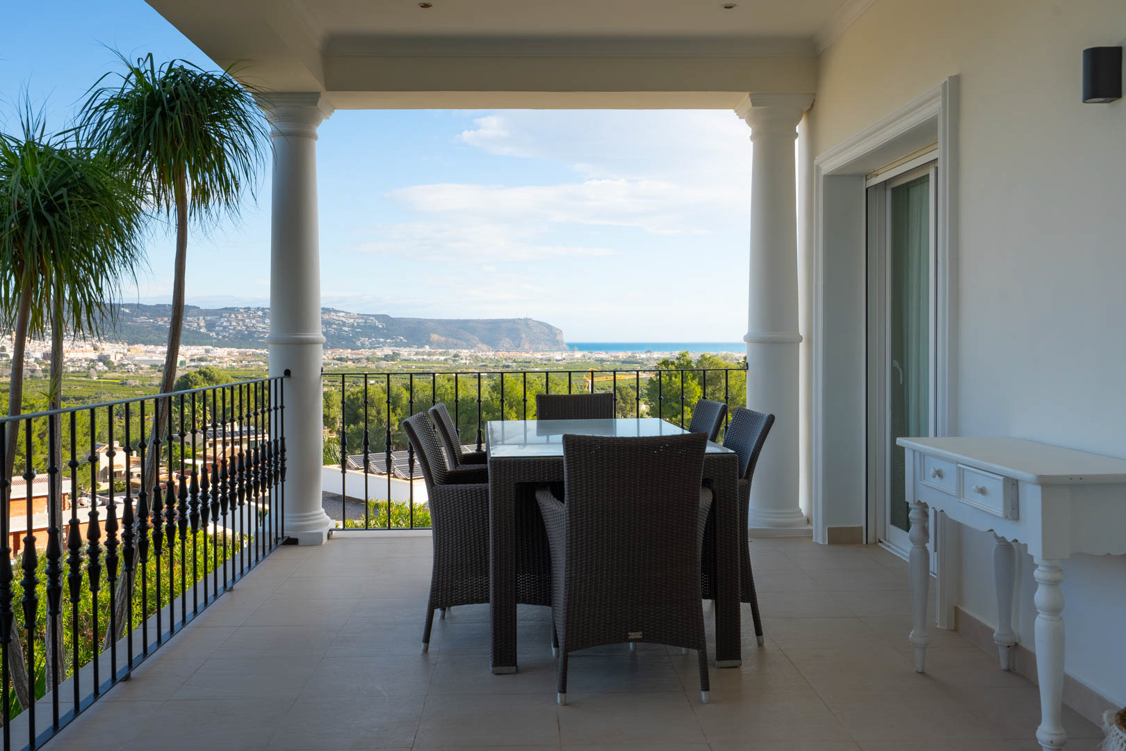 Covered terrace featuring classical columns and wrought iron railings, offering an outdoor dining area with panoramic Mediterranean Sea and valley views.