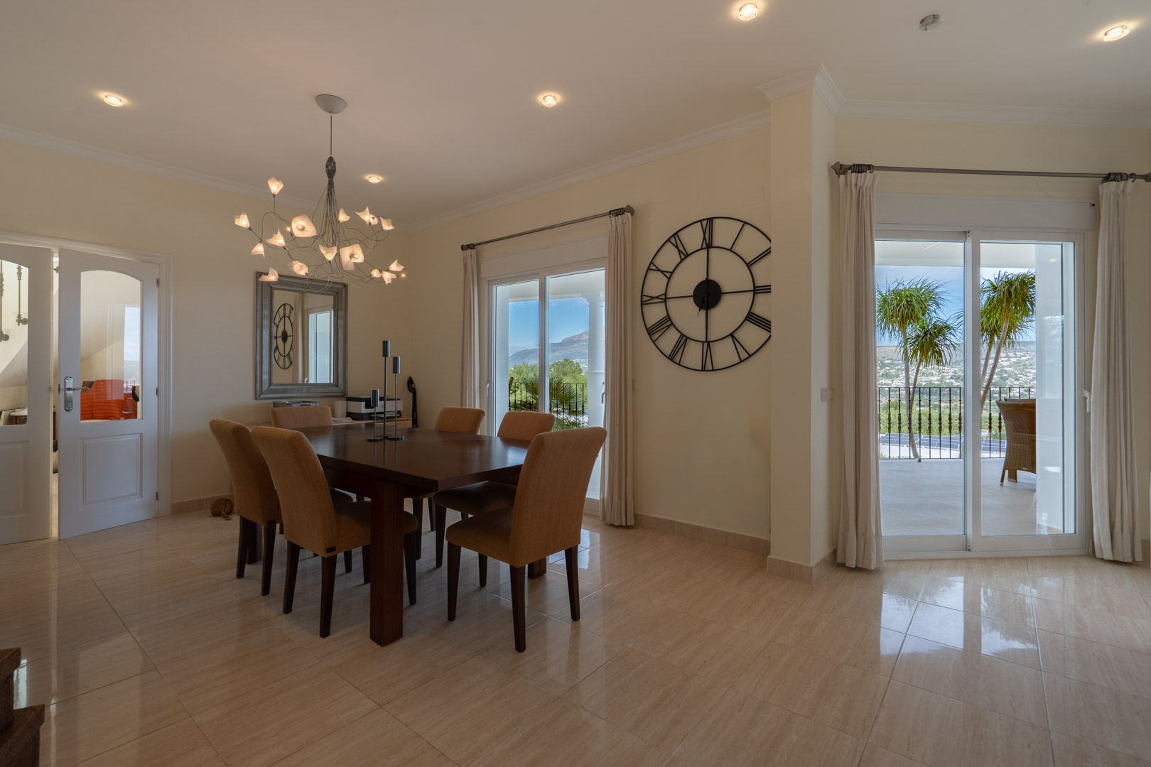 Elegant dining area featuring a dark wood table, designer chandelier, and sliding glass doors that open to a terrace with views of the Montgó mountain.