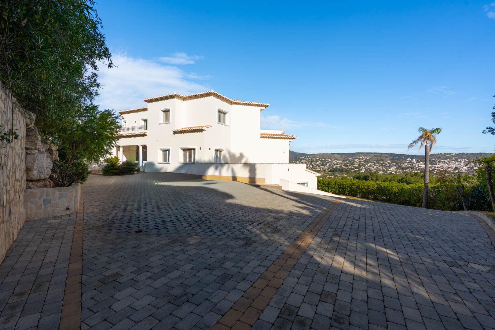 Expansive cobblestone driveway leading to the multi-level white facade, featuring natural stone walls and elevated views of the surrounding valley.