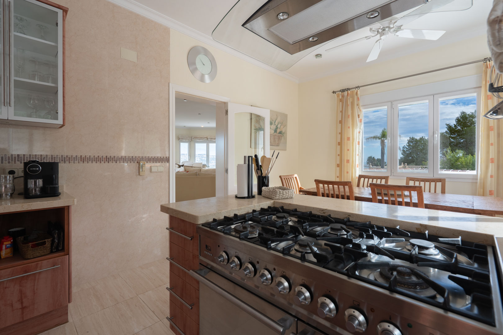 Fully equipped kitchen featuring a professional stainless steel gas range, stone countertops, and a dining area with views of the landscape.
