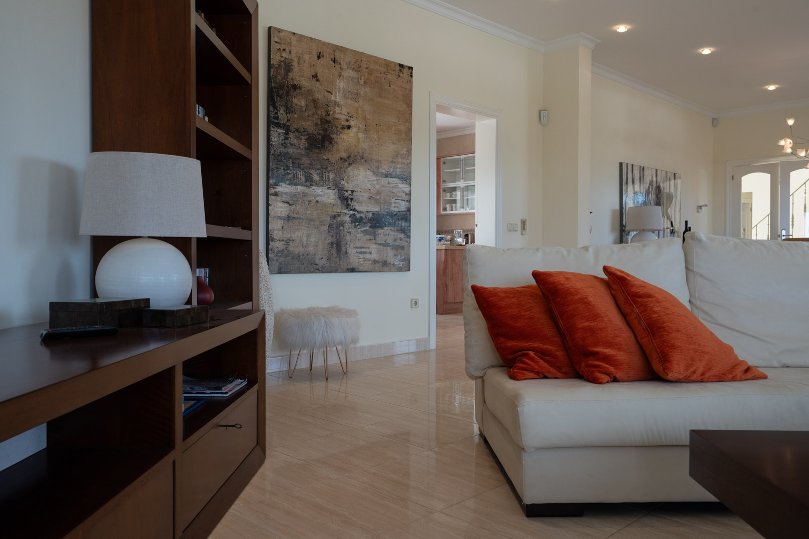 Living area featuring polished tile flooring, a white leather sofa with orange accents, and dark wood cabinetry beside a large abstract canvas.