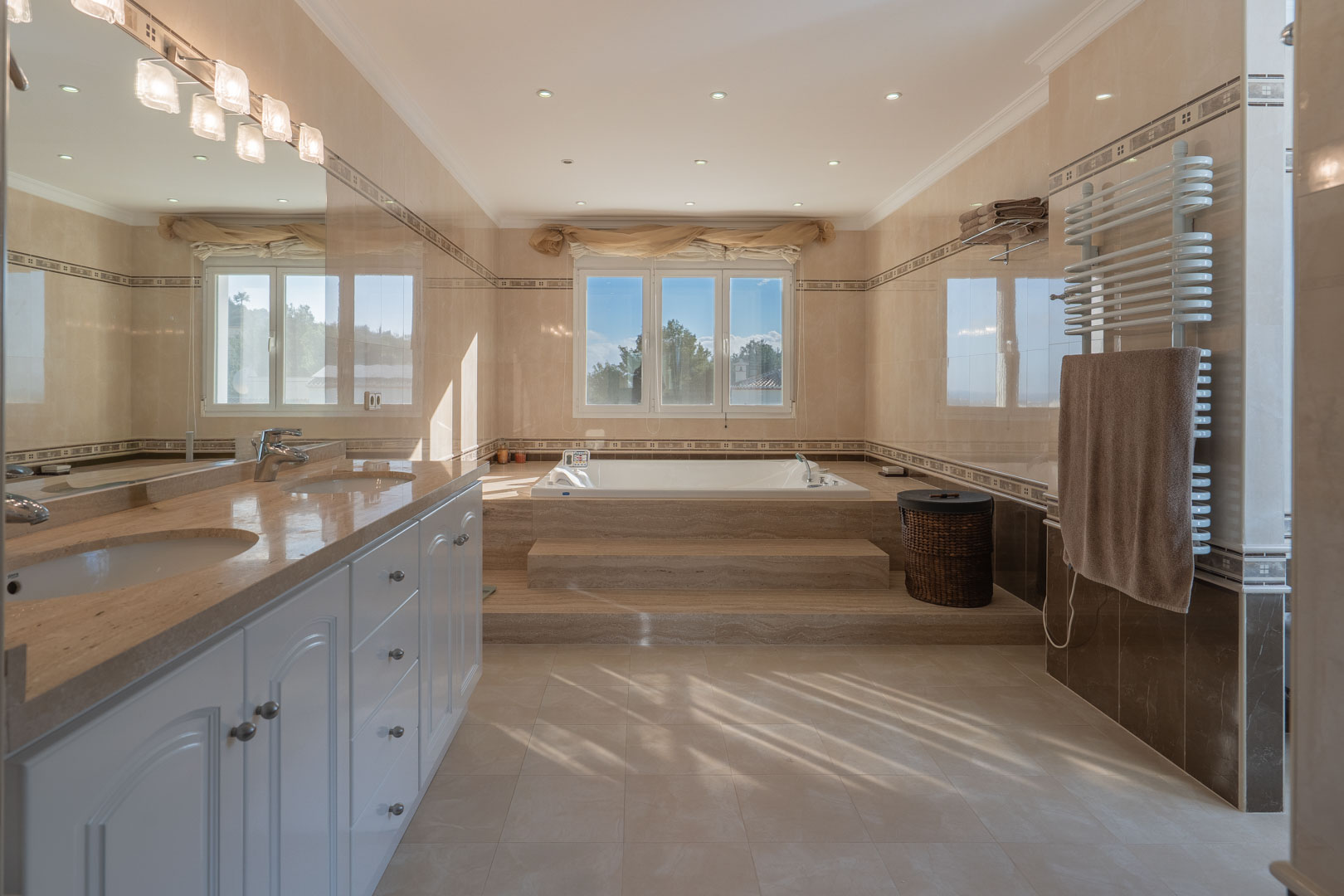 Master bathroom featuring a double marble vanity, an integrated whirlpool tub with stone steps, and elegant recessed lighting throughout the space.