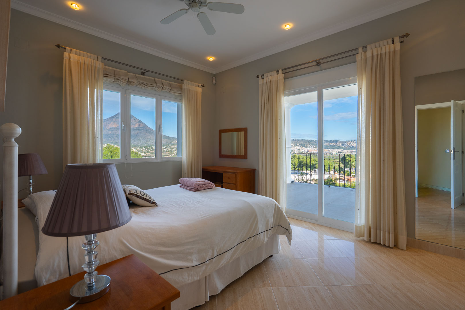 Master bedroom featuring a private terrace, panoramic views of the Montgó mountain, and polished tile flooring. Equipped with a ceiling fan and recessed lighting.