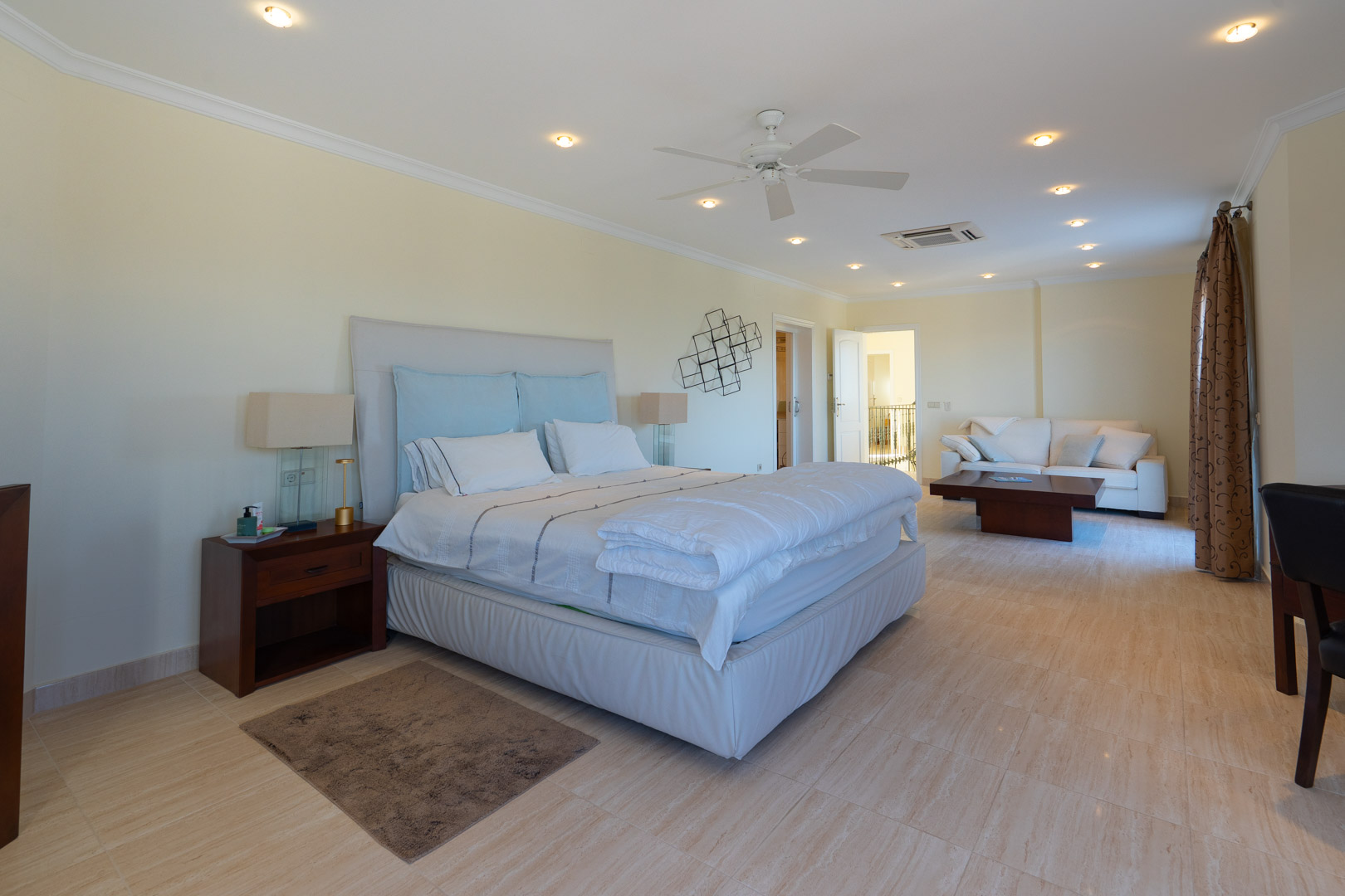 Master bedroom featuring an integrated lounge area, marble flooring, recessed ceiling lighting, and a ceiling fan for climate control.