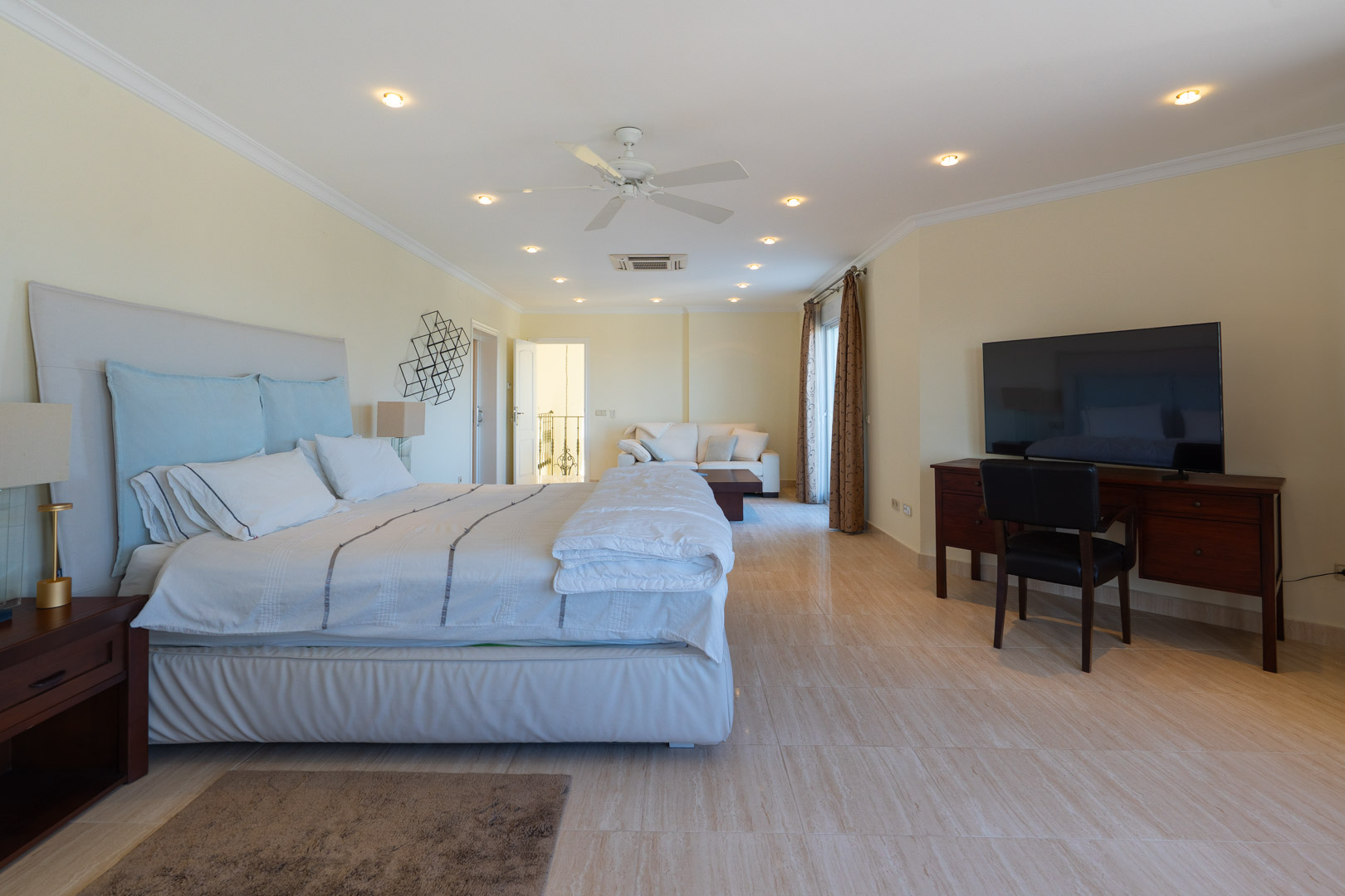 Master suite featuring polished stone floors, an integrated lounge area with a sofa, a wooden workspace, and recessed ceiling lighting.
