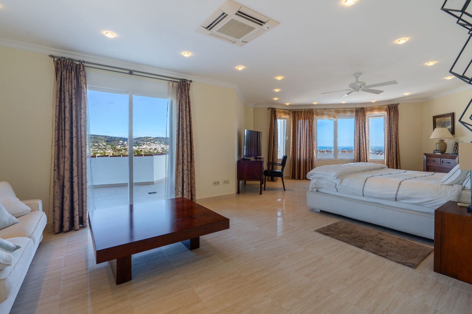 Master suite featuring stone-tiled floors, a seating area, and private terrace access with sea views. Includes classic wood furniture and recessed ceiling lighting.