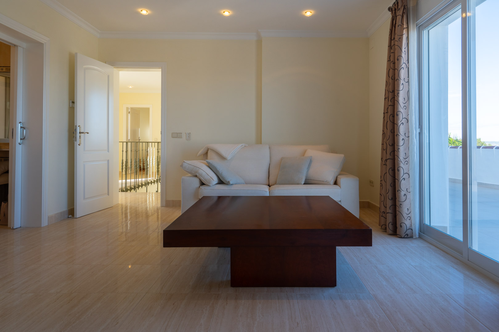Seating area featuring polished marble floors, a dark wood coffee table, and recessed lighting, with access to a private terrace through sliding glass doors.