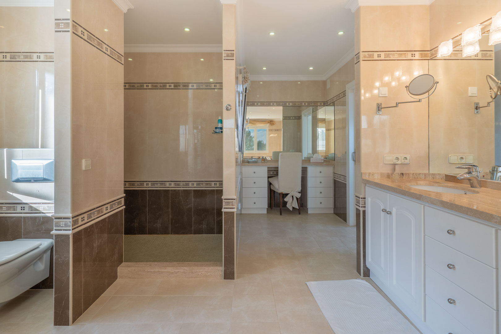 Spacious bathroom featuring two-tone tiling, a walk-in shower, a dedicated dressing table area, and a marble-top vanity with white cabinetry.