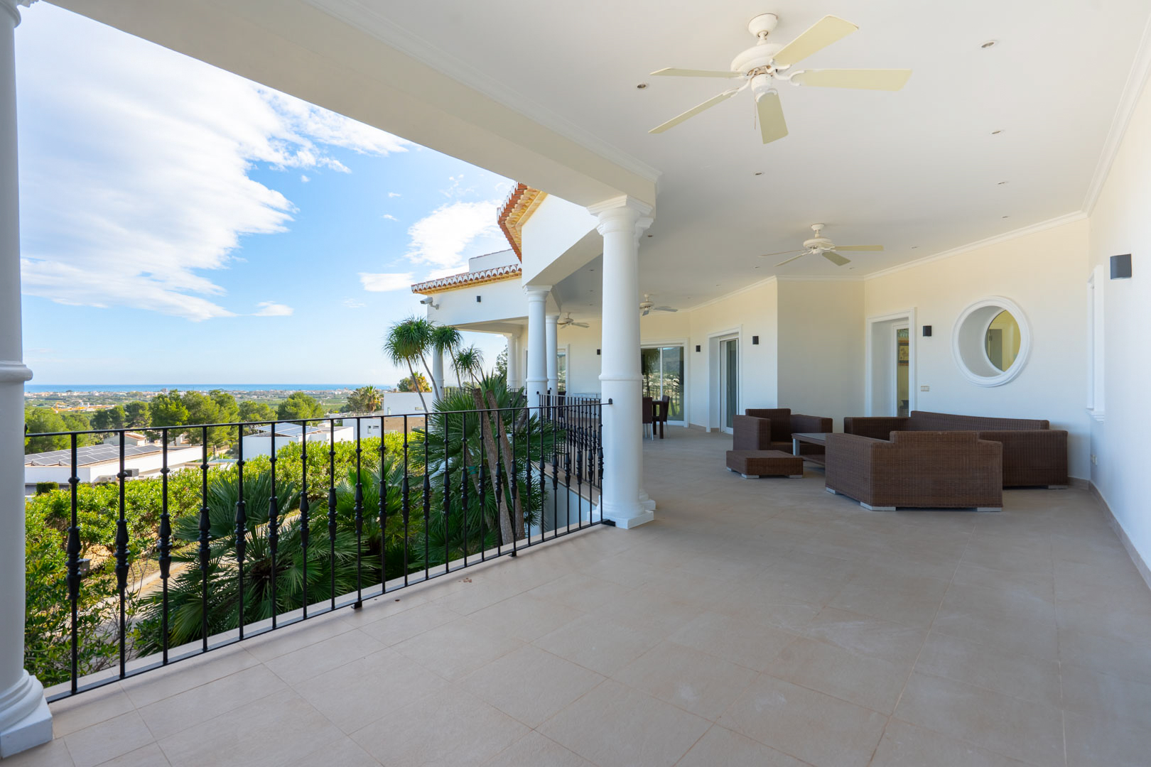 Spacious covered terrace featuring white columns, rattan lounge furniture, and panoramic views of the Mediterranean Sea and coastal landscape.