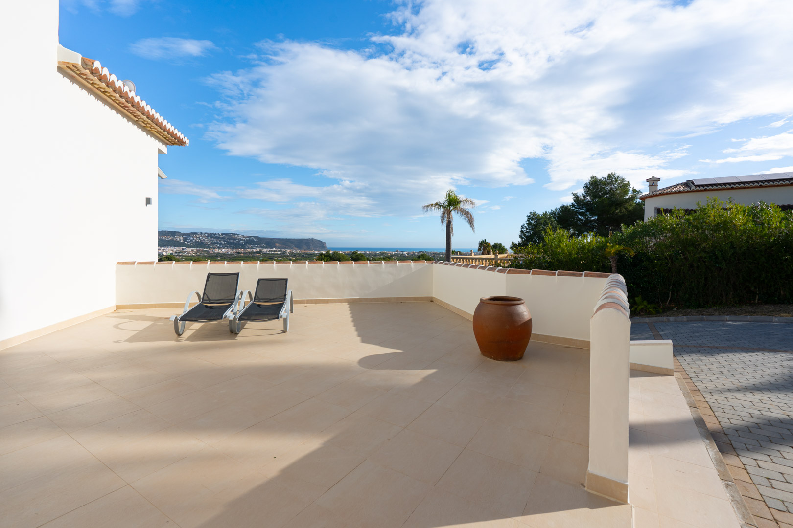 Spacious sun terrace featuring ceramic tiling, two loungers, and a decorative clay pot, offering panoramic views of the Mediterranean coastline.