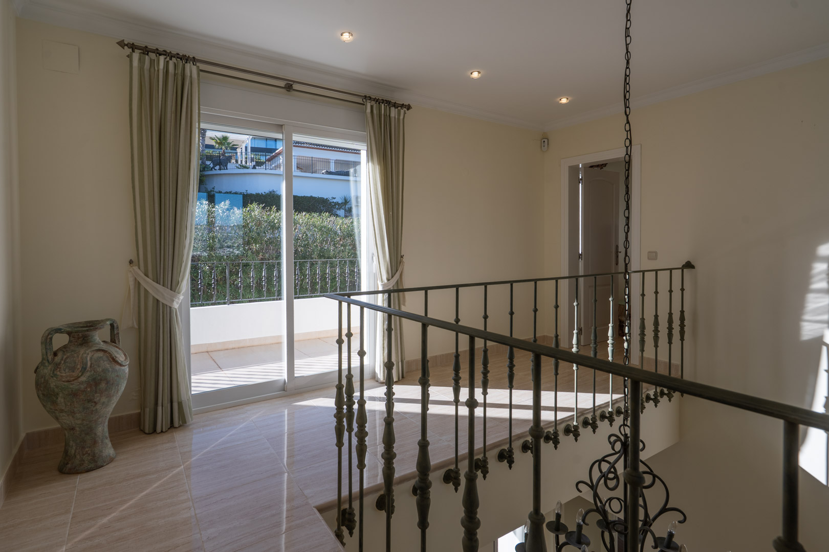 Upper floor landing featuring wrought iron railings, polished tile flooring, and direct access to the private terrace via large sliding doors.