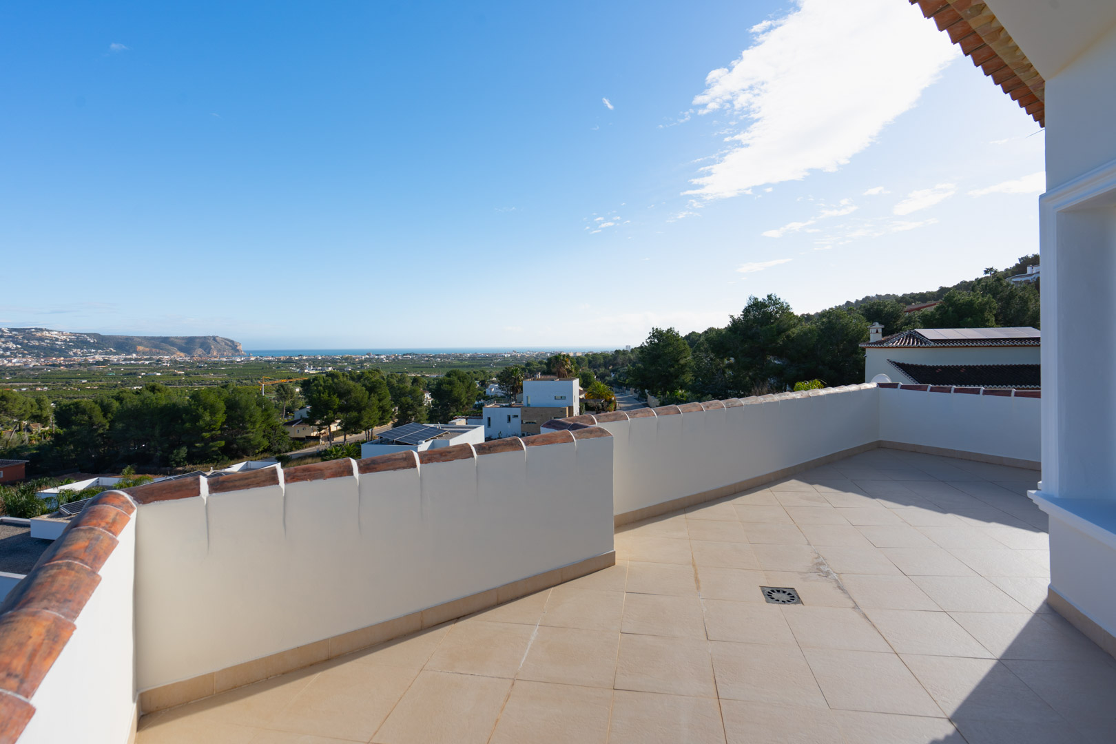 Upper terrace featuring beige ceramic tiling and white parapet walls, providing panoramic views of the Mediterranean coastline and lush valley landscape.