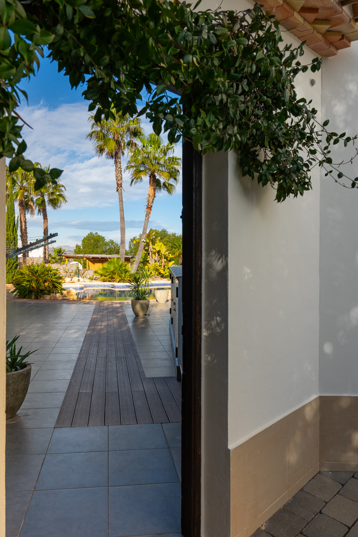 View from the porch toward the pool area, featuring a wooden walkway inset in the tiled terrace and a backdrop of mature palm trees.