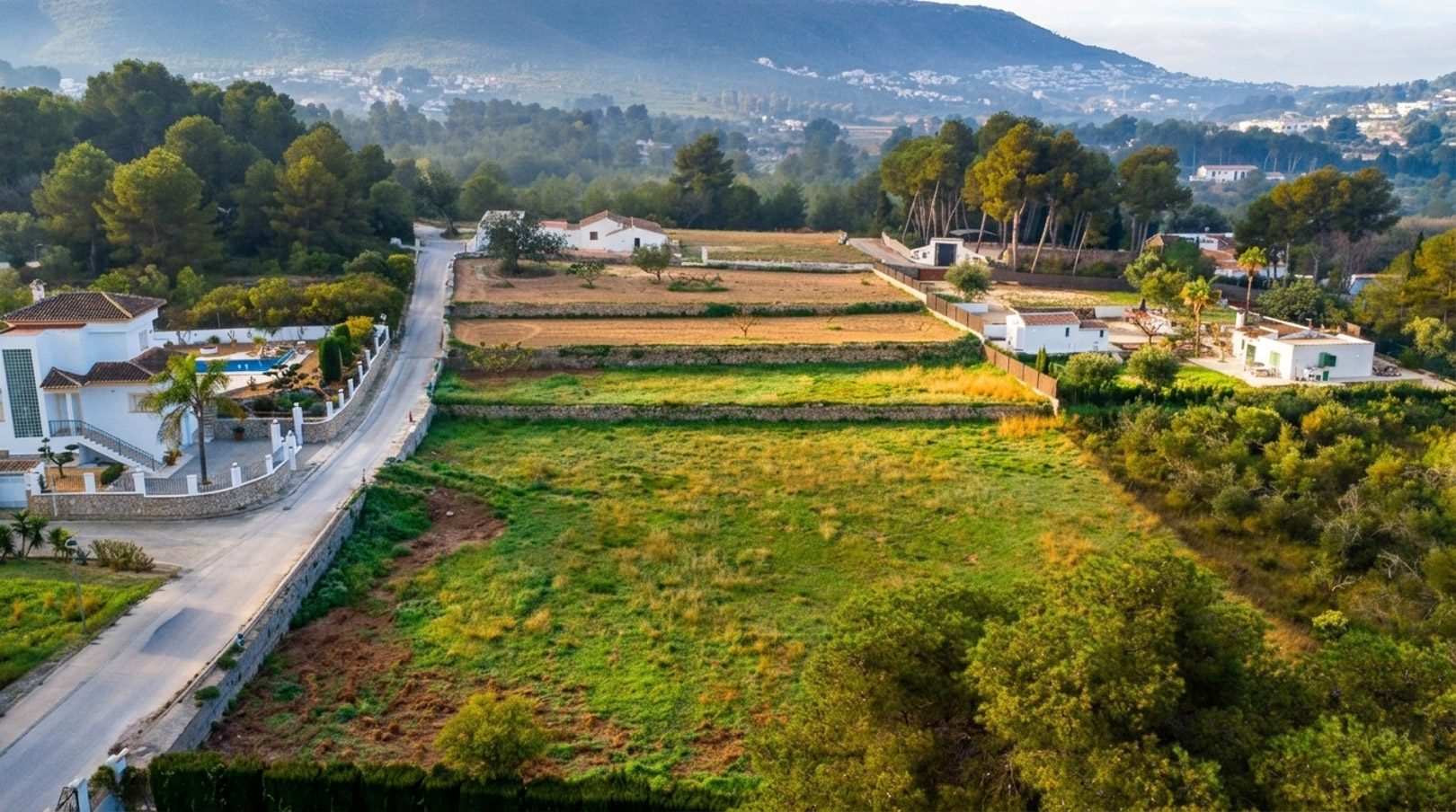 Aerial perspective of the rustic plot showing traditional stone terraces, surrounded by lush pine trees and scenic mountain views in Jávea.