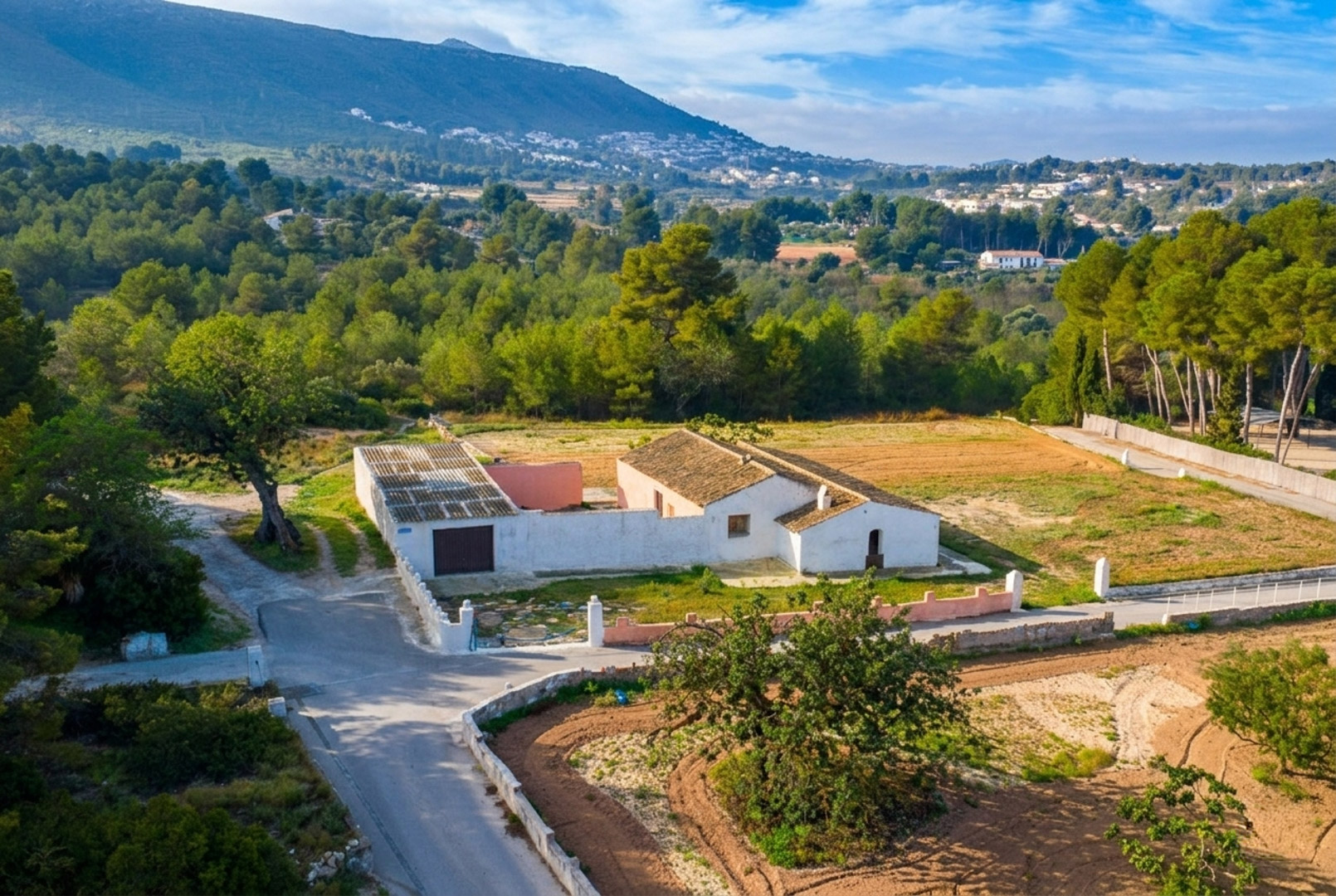 Aerial view of the traditional white-walled finca and its outbuildings, set on a flat rustic plot surrounded by Mediterranean pine forests and mountain views.