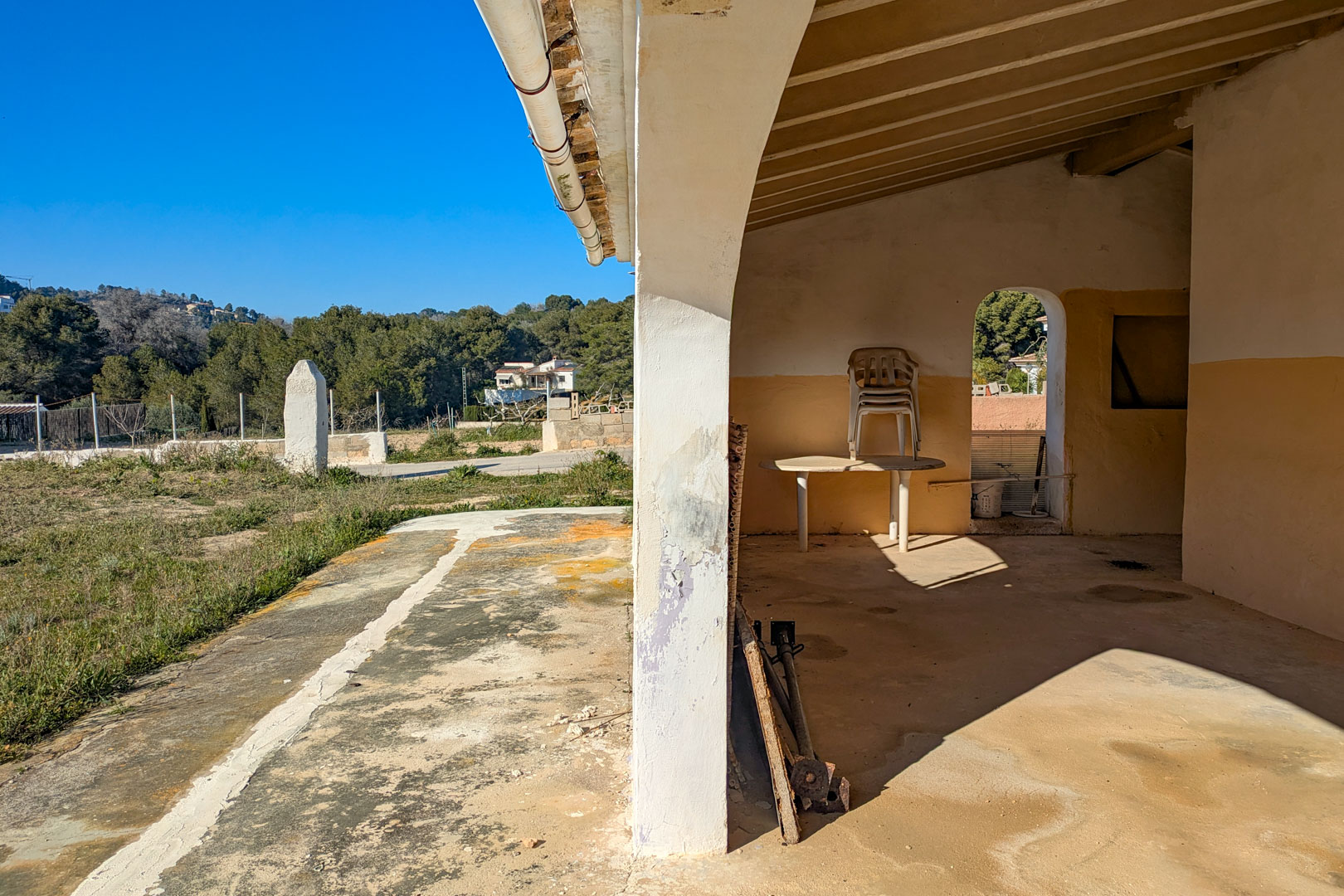Covered porch featuring exposed wooden ceiling beams and arched pillars, overlooking the expansive rustic plot and natural landscape.