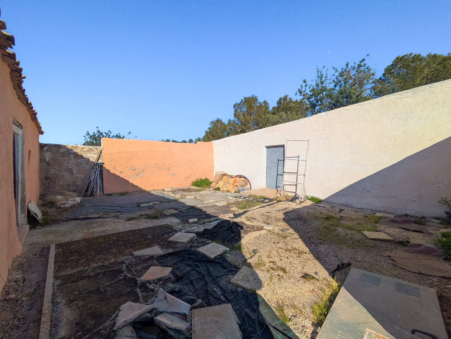 Enclosed courtyard with high perimeter walls, a blue utility door, and ground surfaces prepared with protective sheeting for future renovation.