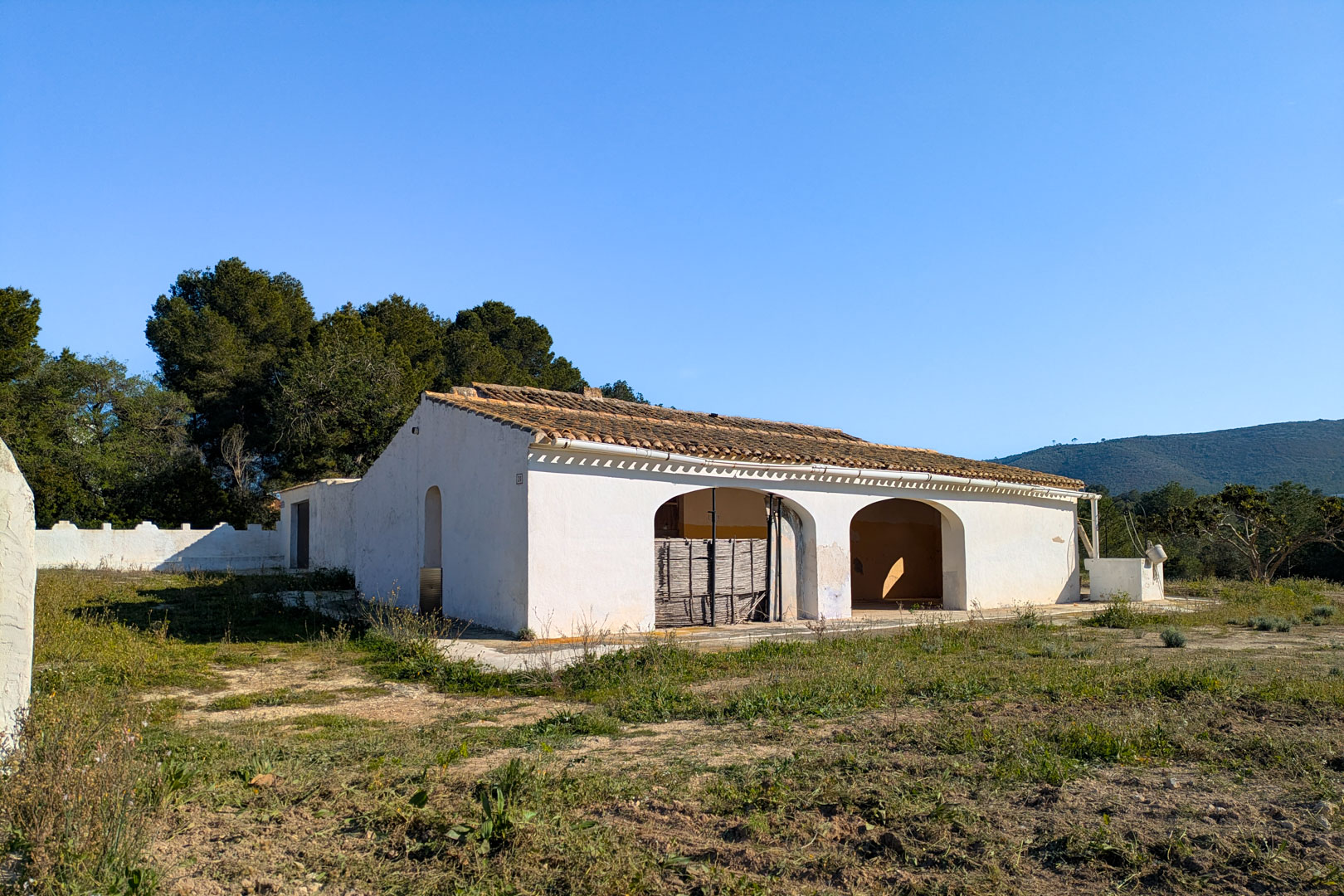 Exterior view of the traditional finca featuring an arched naya and clay tile roof, set on a large rustic plot with mountain views.
