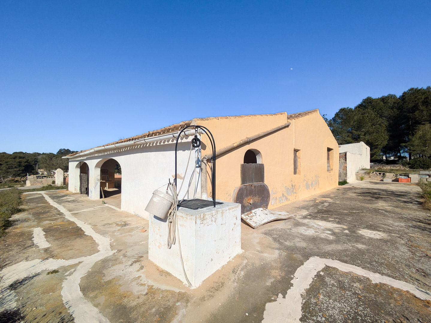 Exterior view of the traditional finca featuring an arched porch, a stone well with a pulley system, and a spacious sun-drenched patio.